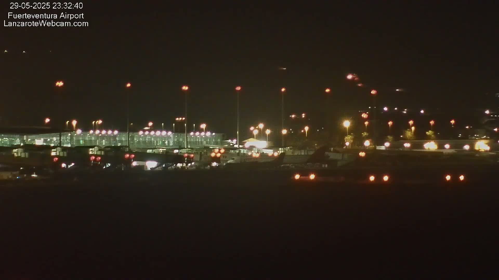 A nighttime view of an airport terminal and tarmac, illuminated by numerous lights.