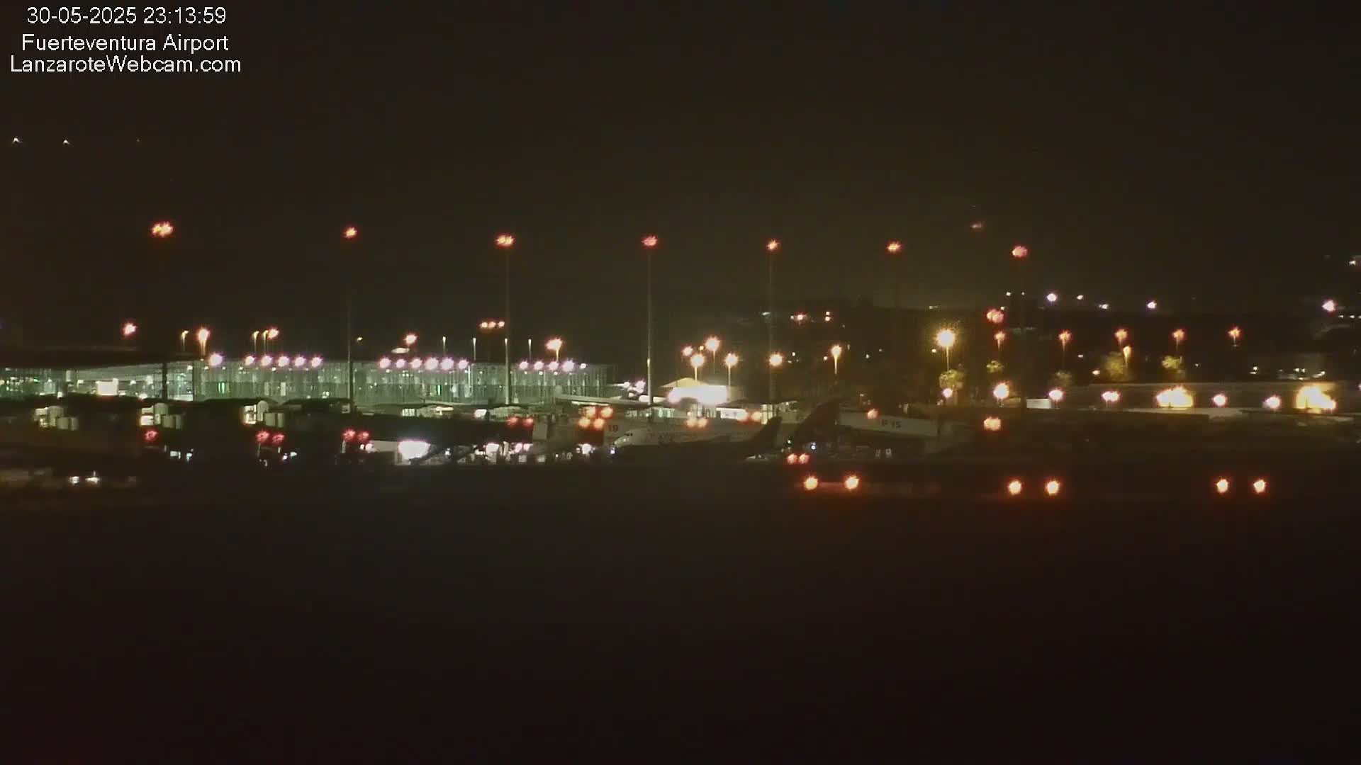 A nighttime long shot of an airport terminal and several airplanes on the tarmac, illuminated by numerous lights under a clear, dark sky.