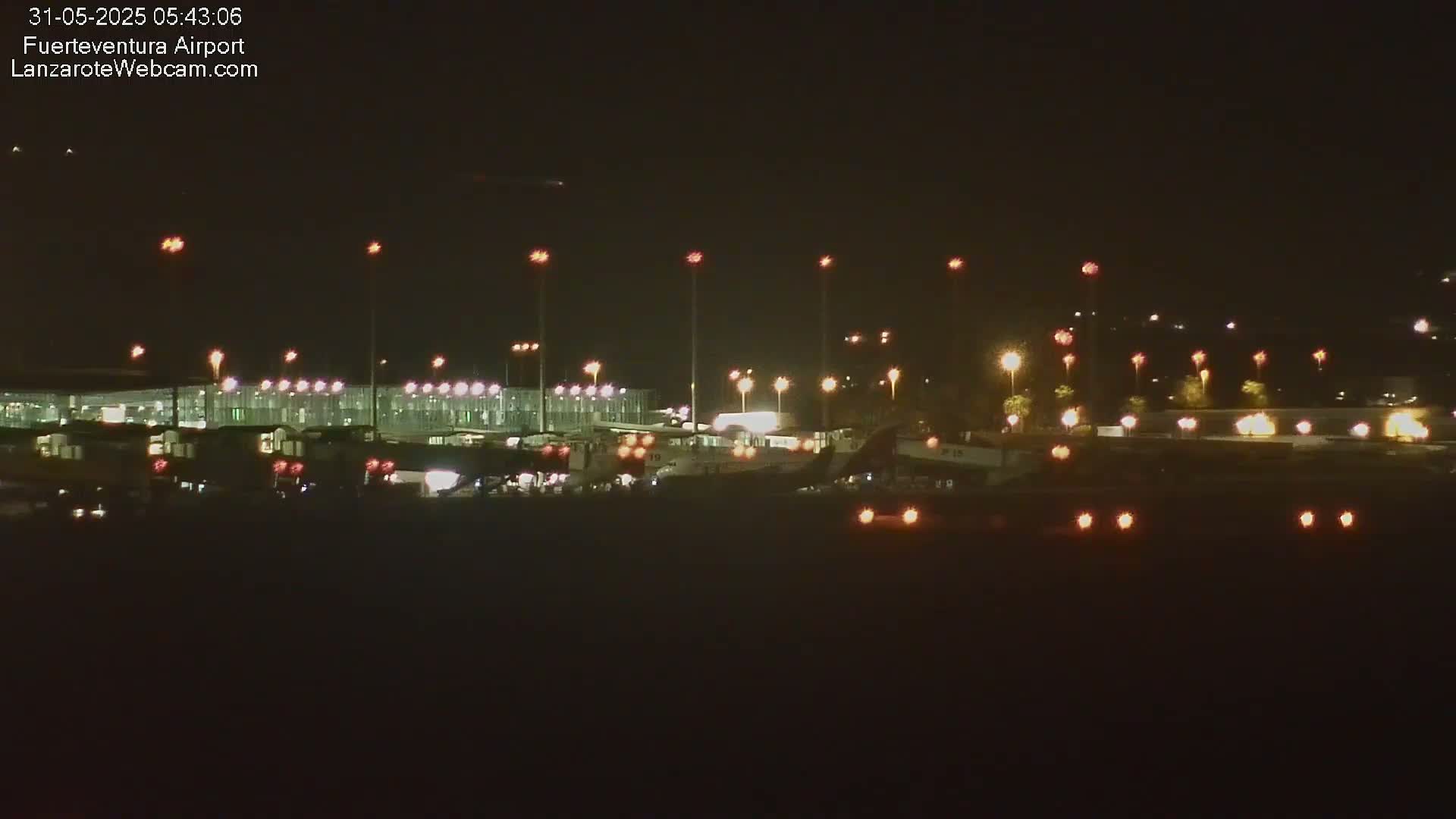 A nighttime view of an airport tarmac with several planes and buildings illuminated by numerous lights.