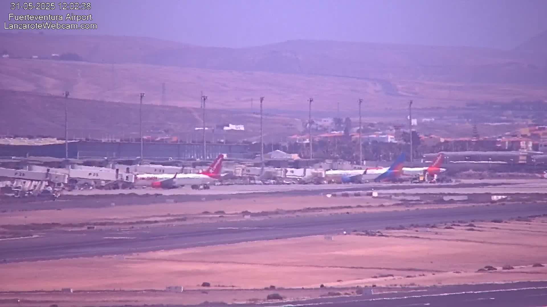 Several airplanes are parked at an airport tarmac under hazy conditions.