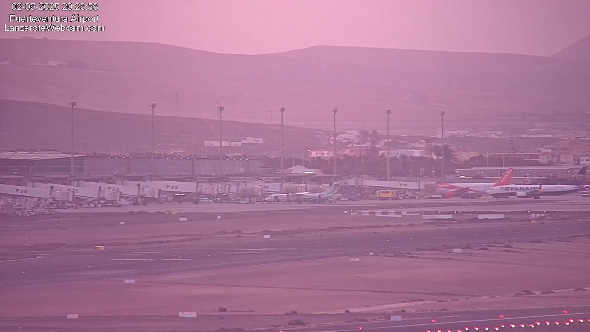 Under a hazy pink sky, several airplanes are parked at an airport terminal with jet bridges connected.