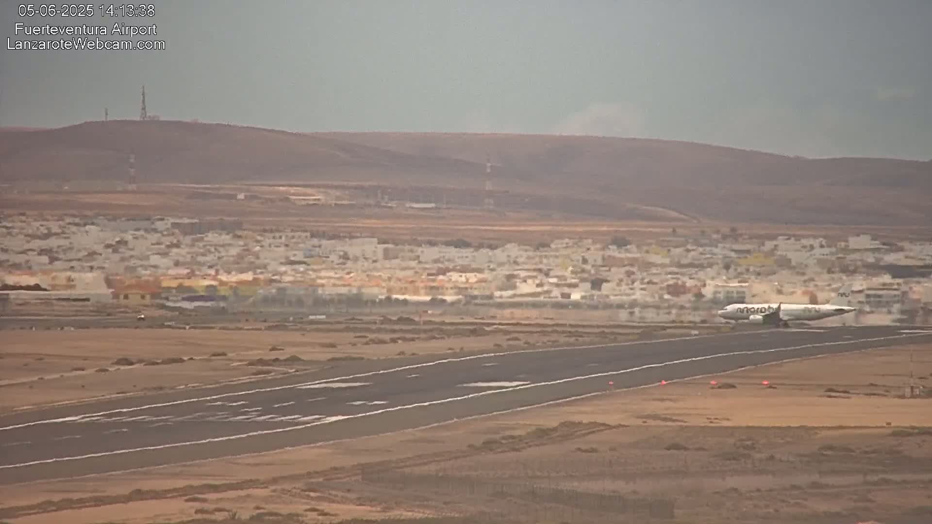 An airplane taxis on a runway near a town under hazy conditions.