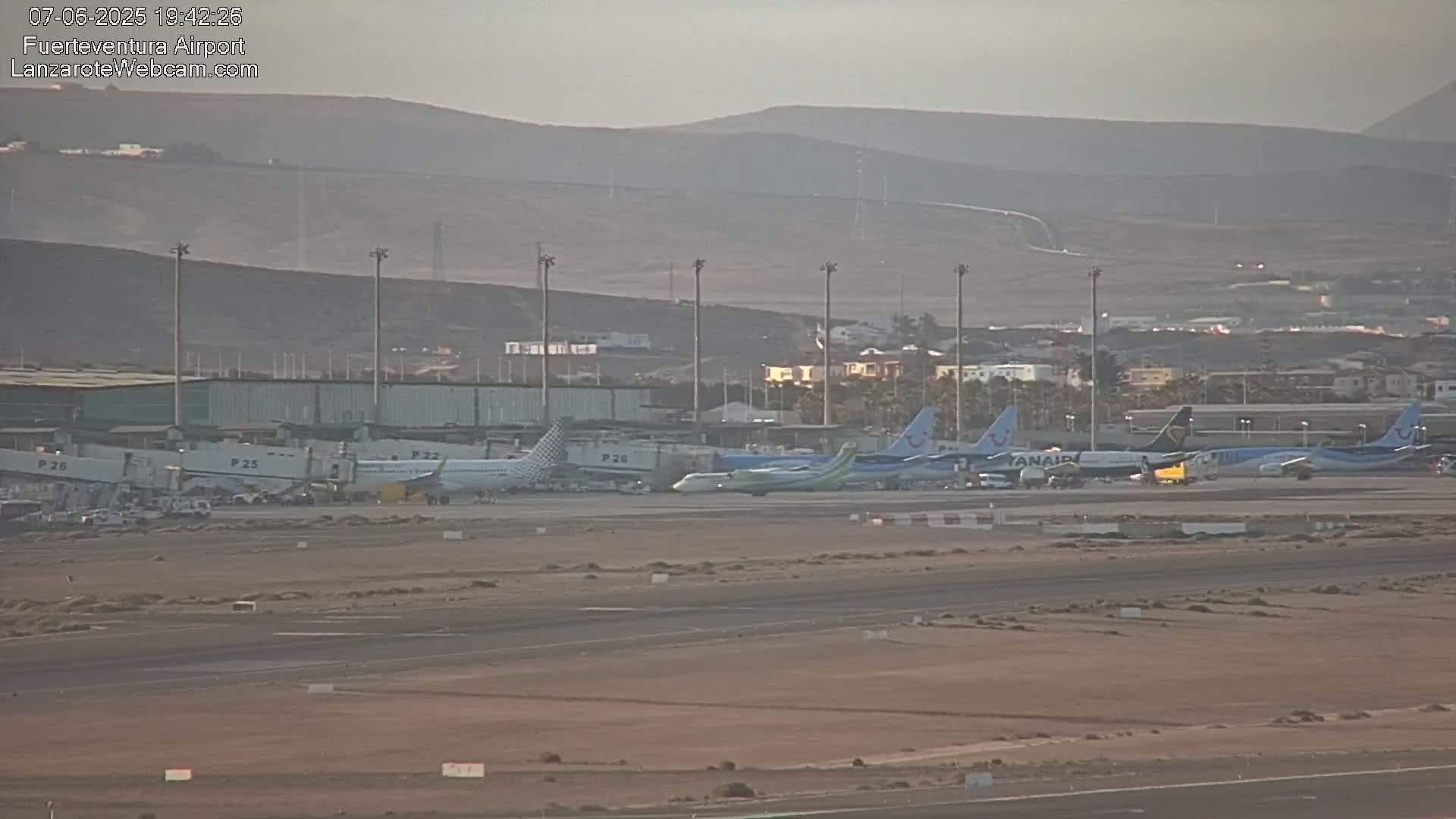 Several airplanes are parked at an airport on a hazy day, with hills visible in the background.
