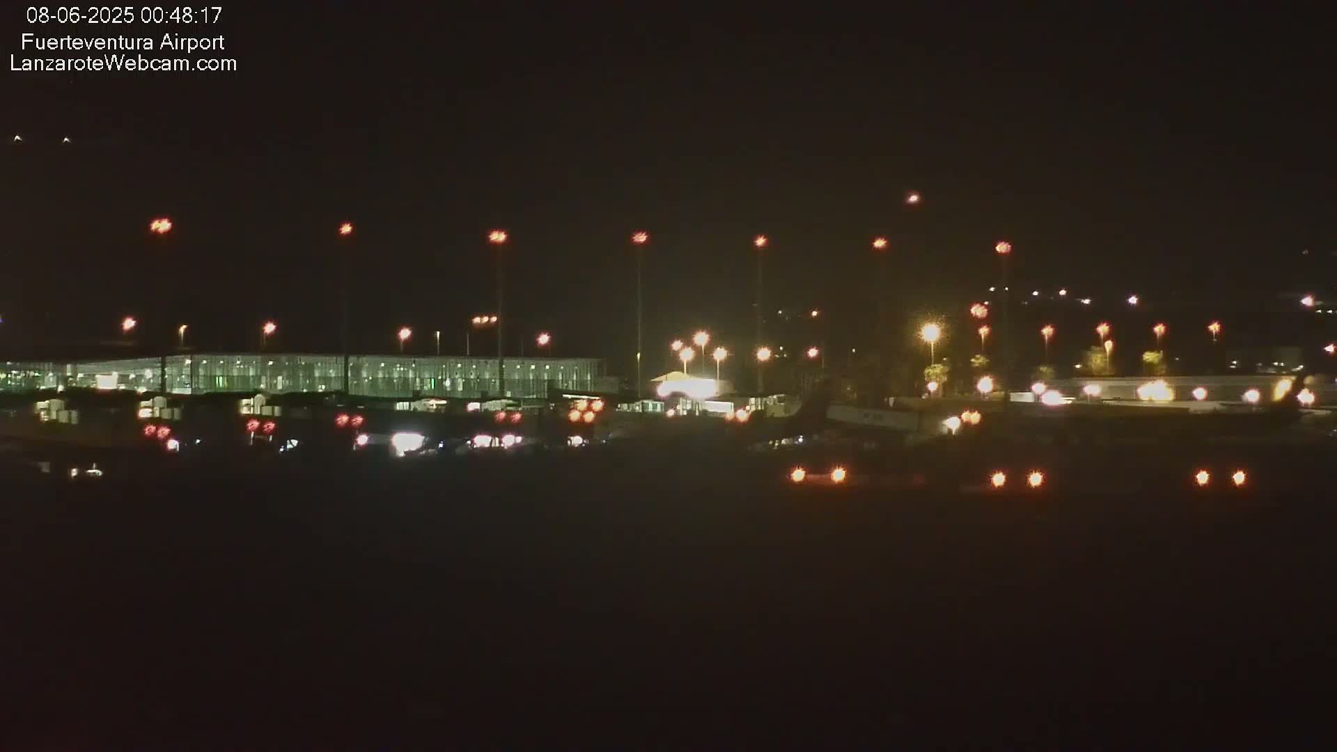 A nighttime view of an airport terminal building and tarmac, illuminated by numerous lights.