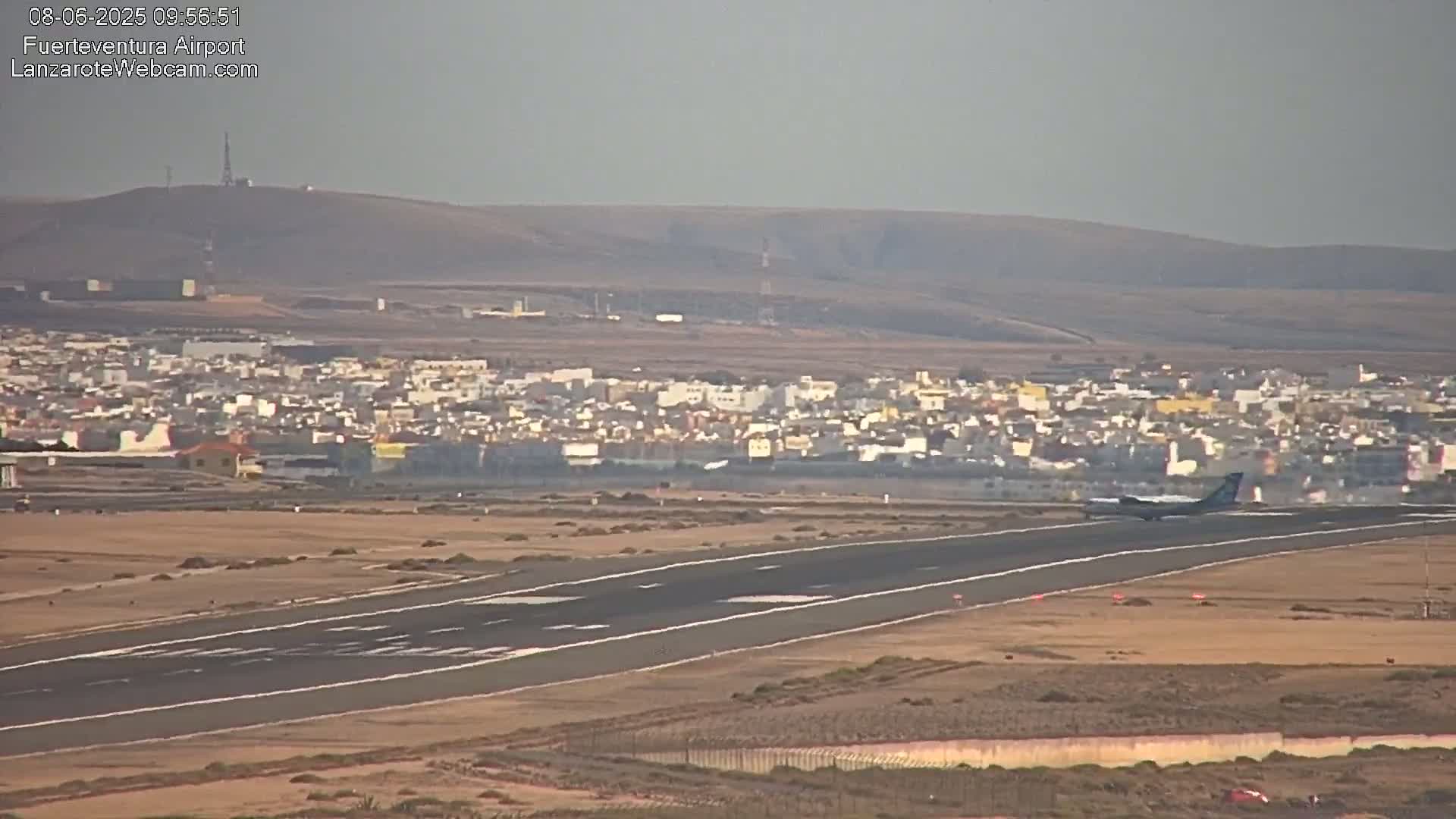 A plane lands on a runway near a town under hazy conditions.