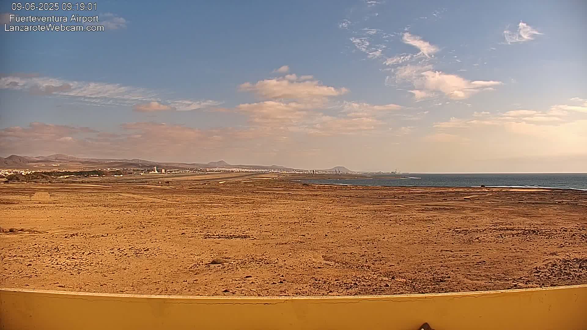 A flat, sandy expanse stretches to a distant coastline under a partly cloudy sky.
