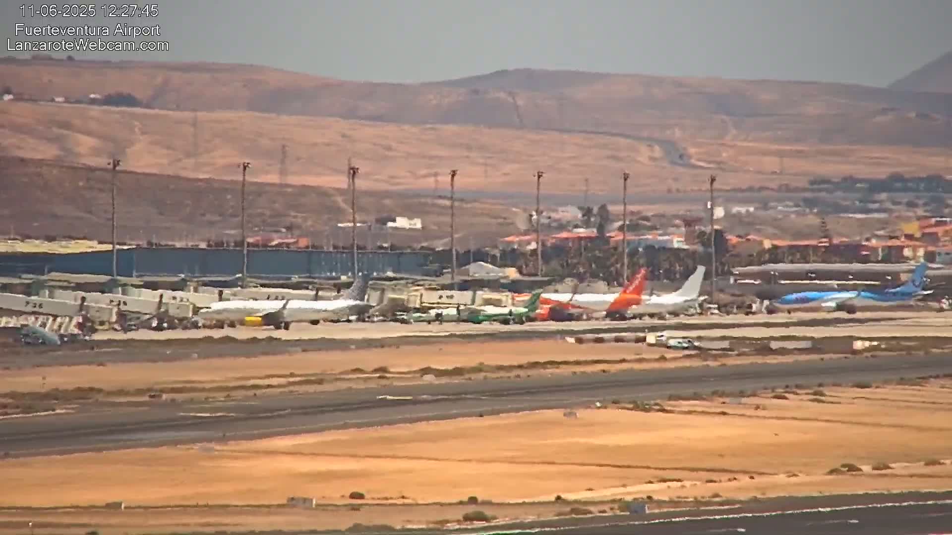 Several airplanes are parked on an airport tarmac under hazy conditions with distant, light brown hills in the background.