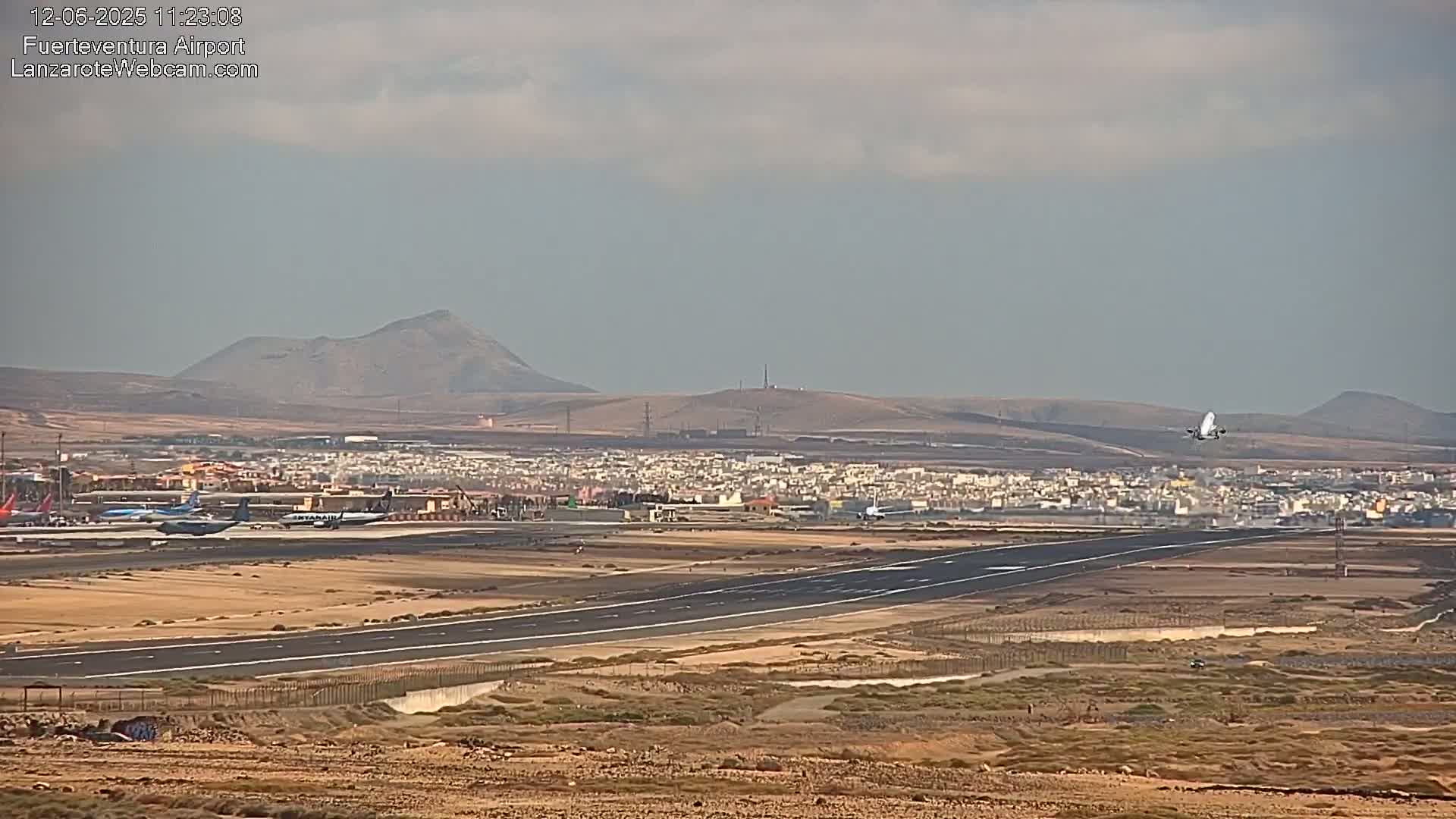 A plane takes off from an airport runway next to a town, under a mostly cloudy sky.