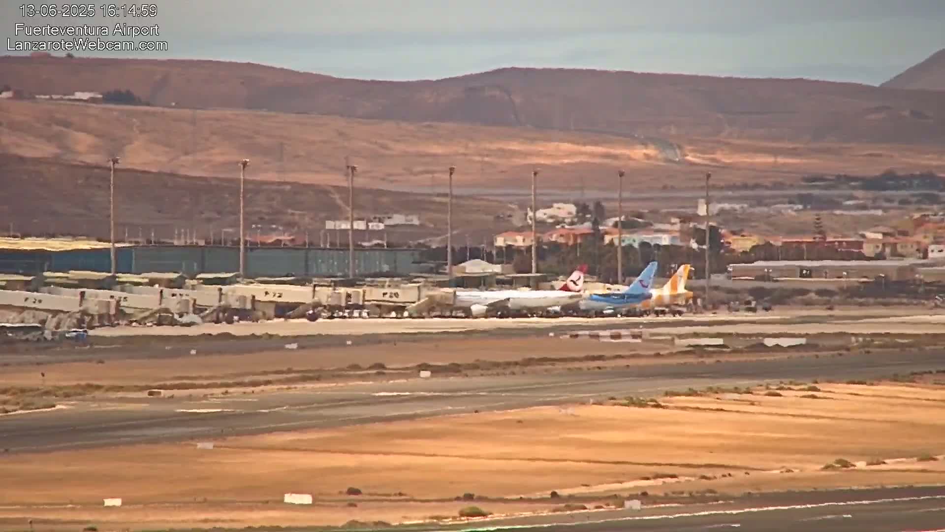 Two airplanes are parked at an airport tarmac near a building under a hazy sky, with brown hills visible in the distance.