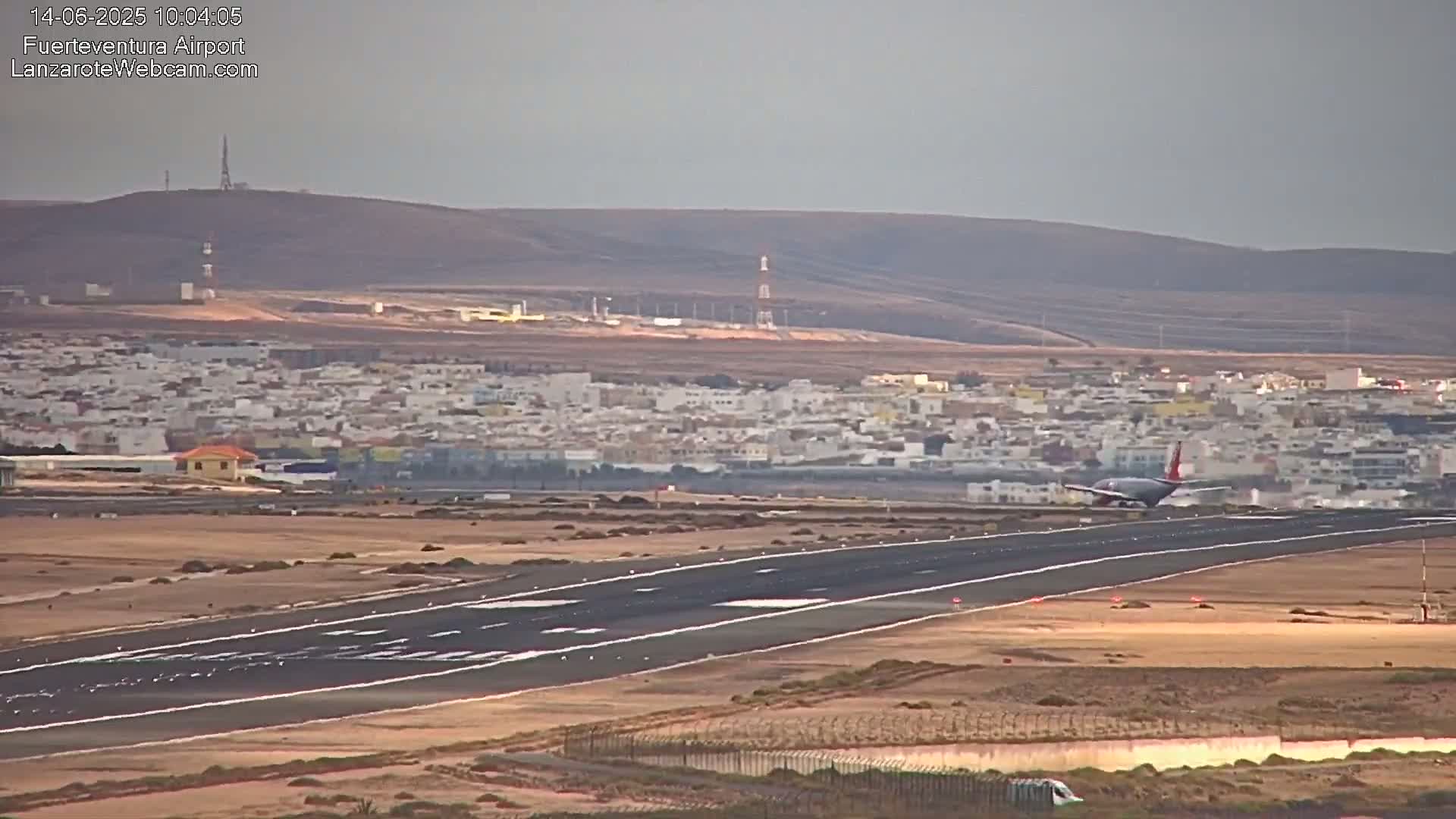 A passenger plane lands on a runway at an airport near a town, under a hazy sky.