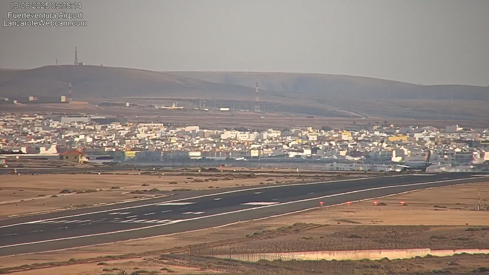 A plane lands on a runway at an airport near a town under hazy conditions.