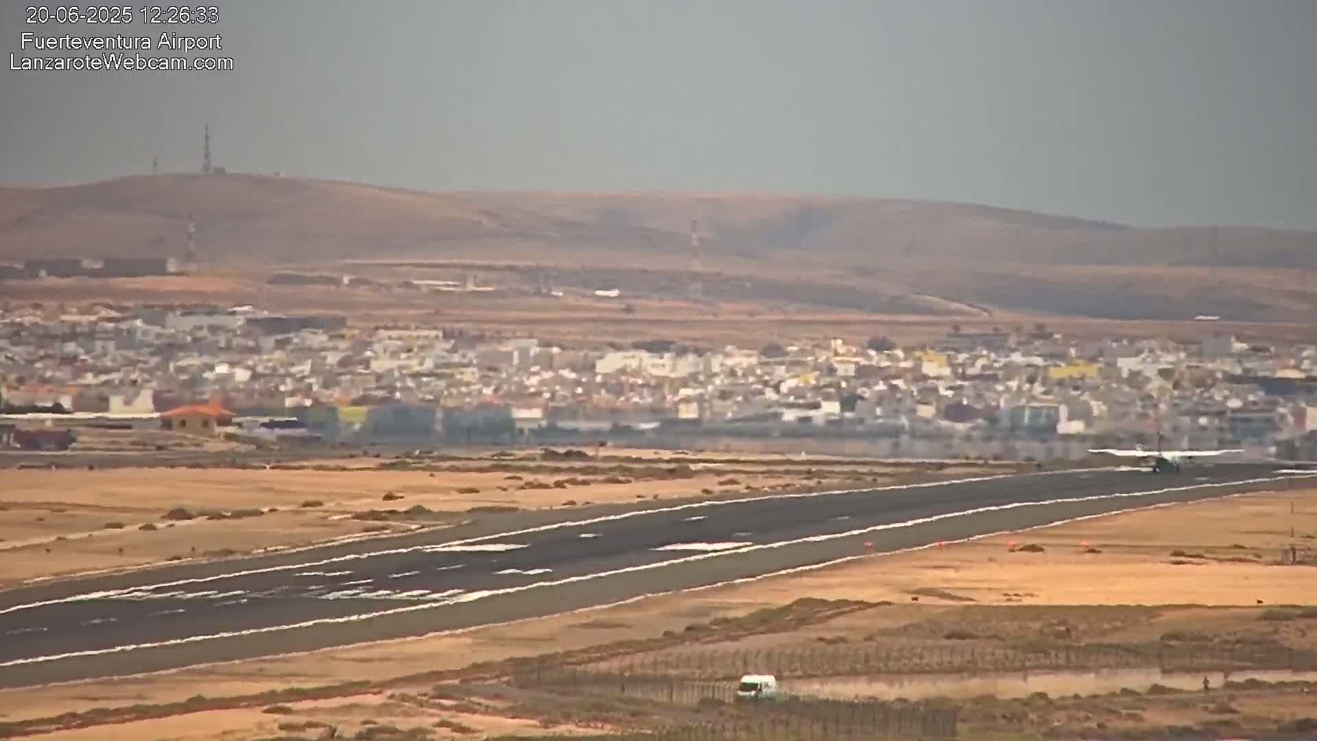 A small airplane lands on a runway near a town under hazy conditions.