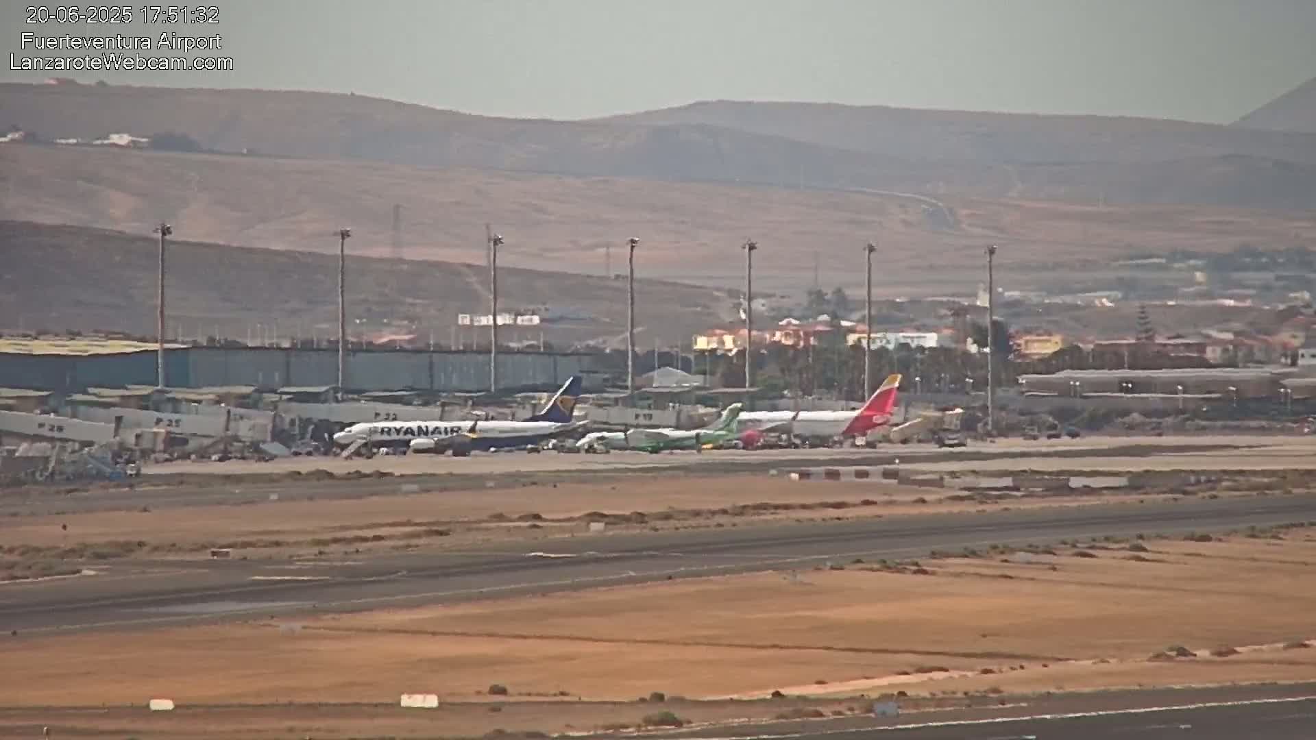 Several airplanes are parked at an airport tarmac on a hazy day, with a mountainous landscape visible in the background.