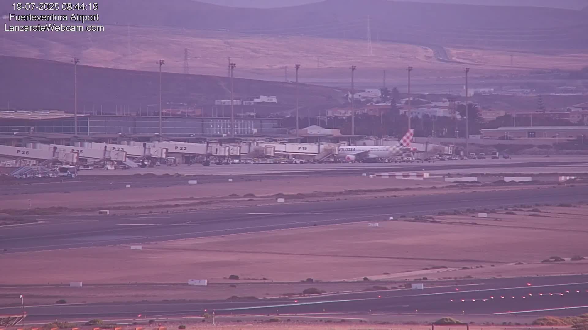 An airplane is parked at a gate of a large airport on a hazy, dusky day.