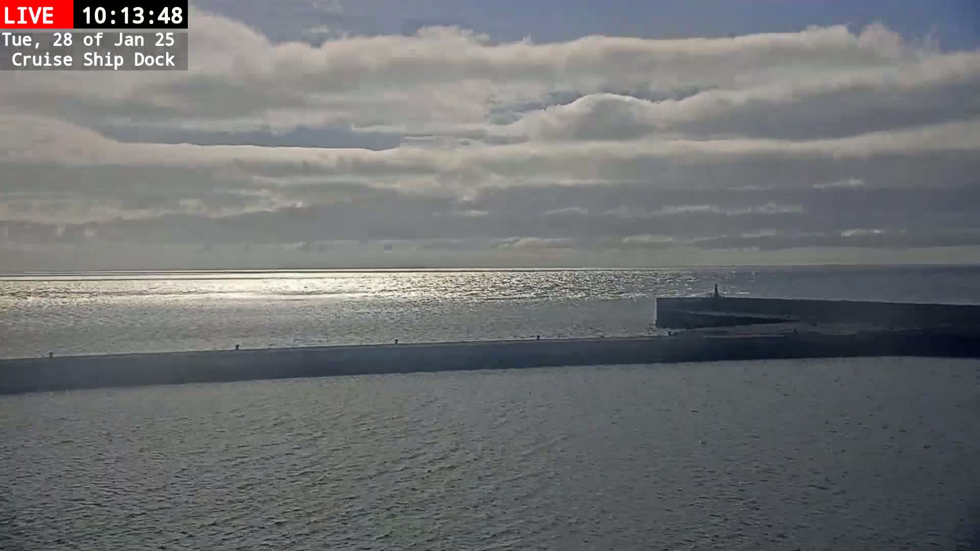 A long, low breakwater extends into a calm sea under a mostly cloudy sky.