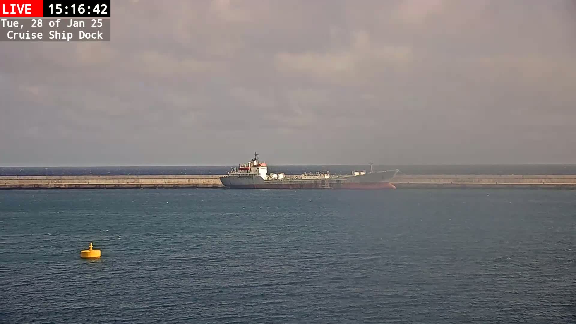 A large ship is docked at a seawall under a mostly cloudy sky.