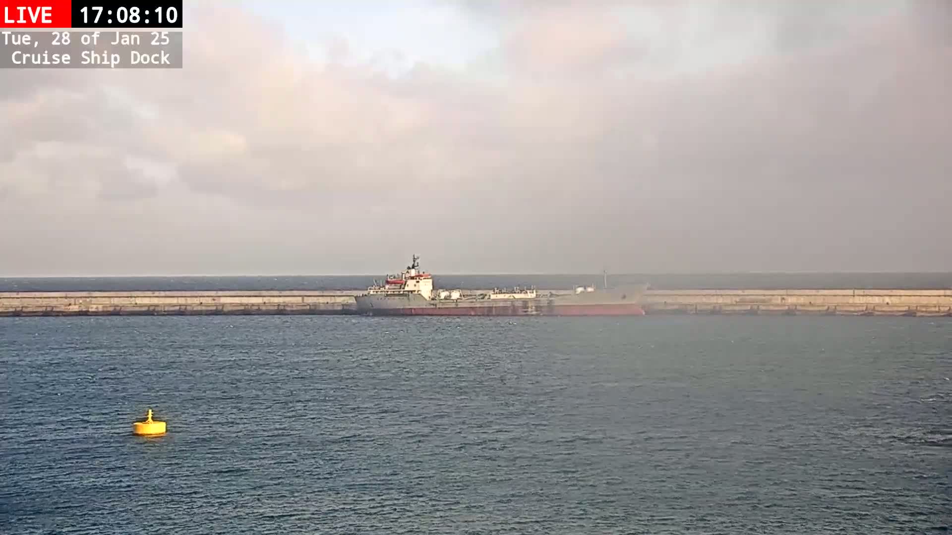 A large ship is docked at a concrete pier on a cloudy day.