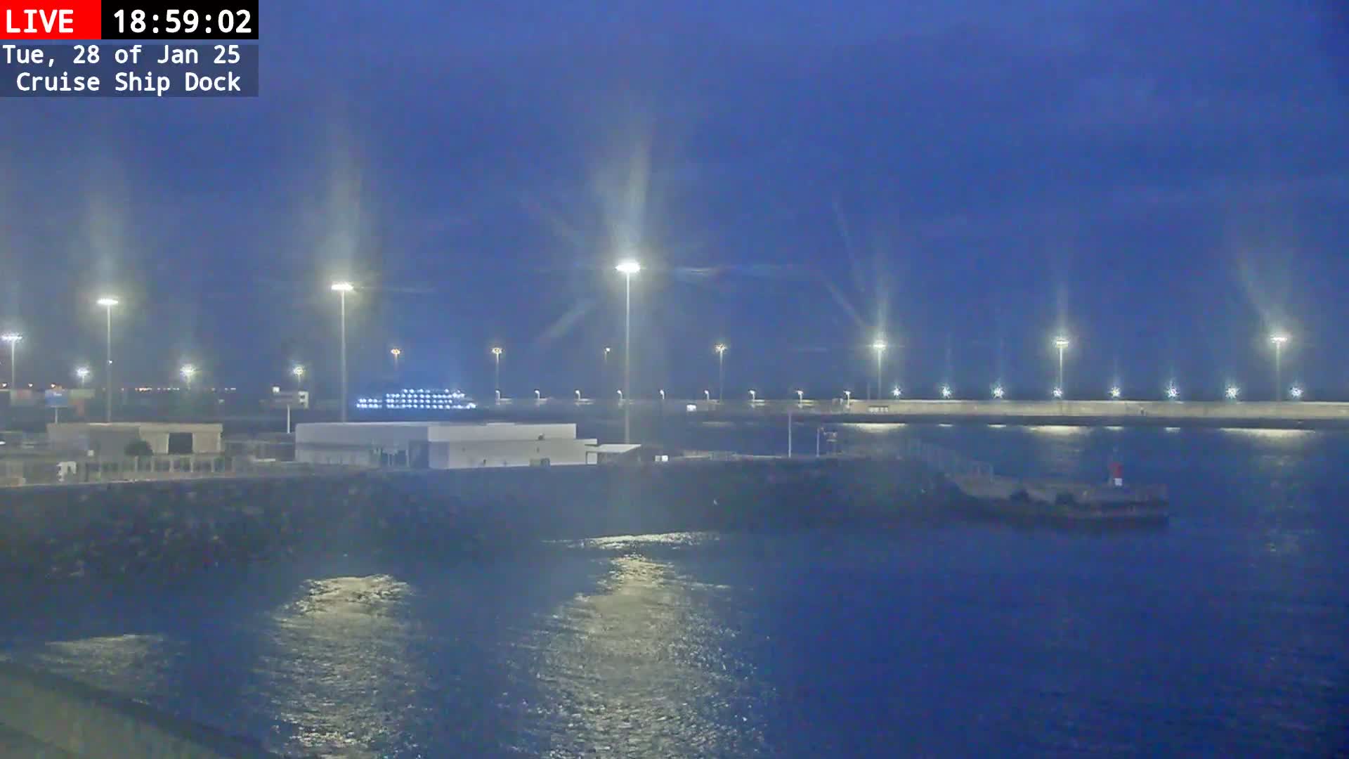 A dark-blue, nighttime scene shows a cruise ship dock illuminated by tall lights, with a small vessel in the water.