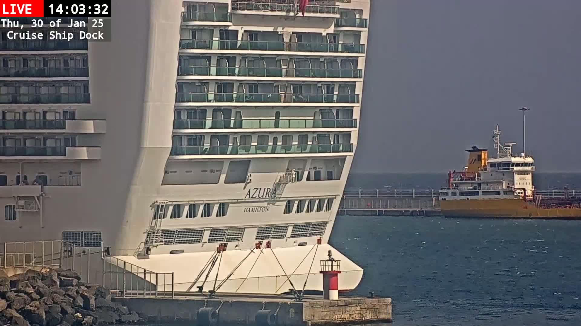A large cruise ship is docked next to a smaller cargo ship on a partly cloudy day.