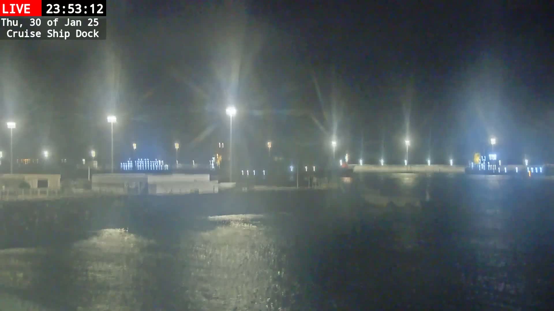 A nighttime view of a cruise ship dock illuminated by bright lights, reflecting on the dark water.