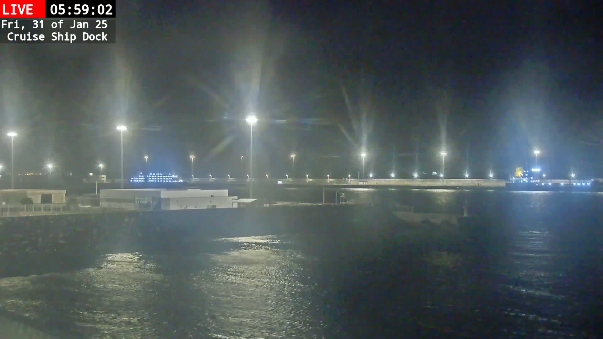 A nighttime view of a cruise ship docked at a port, with somewhat choppy water visible in the foreground.