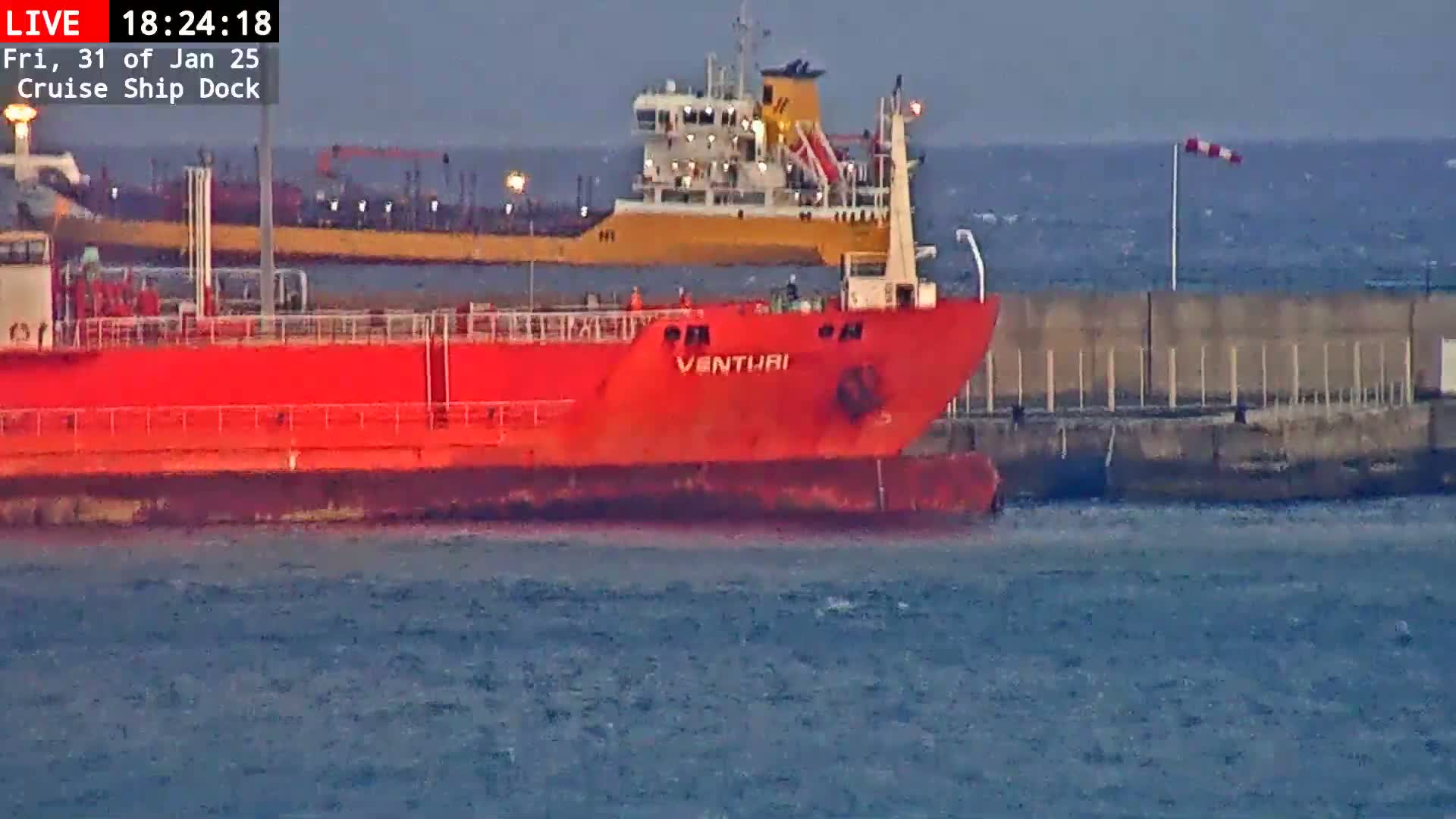 A red ship named Venturi is docked next to a yellow ship in choppy water, with a windsock indicating windy conditions.