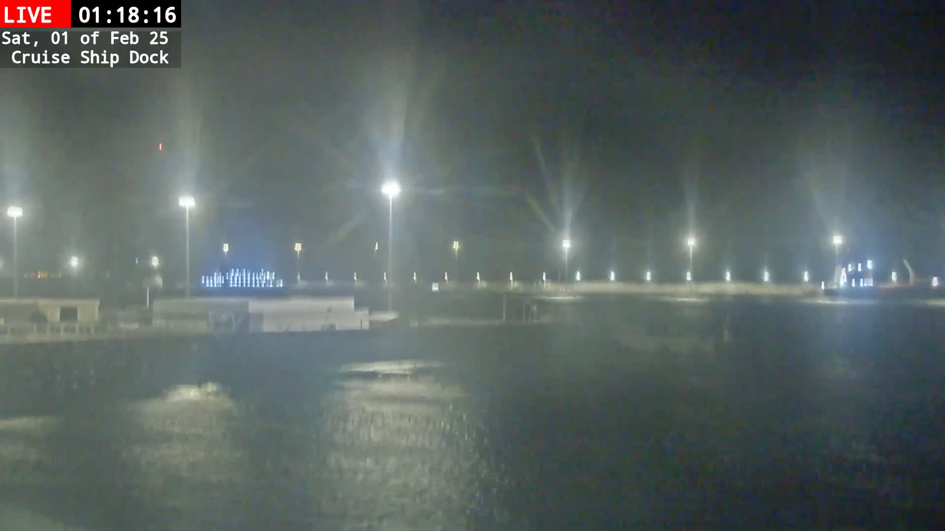 A nighttime view of a cruise ship dock with many lights illuminating a dark, somewhat choppy body of water under a hazy sky.