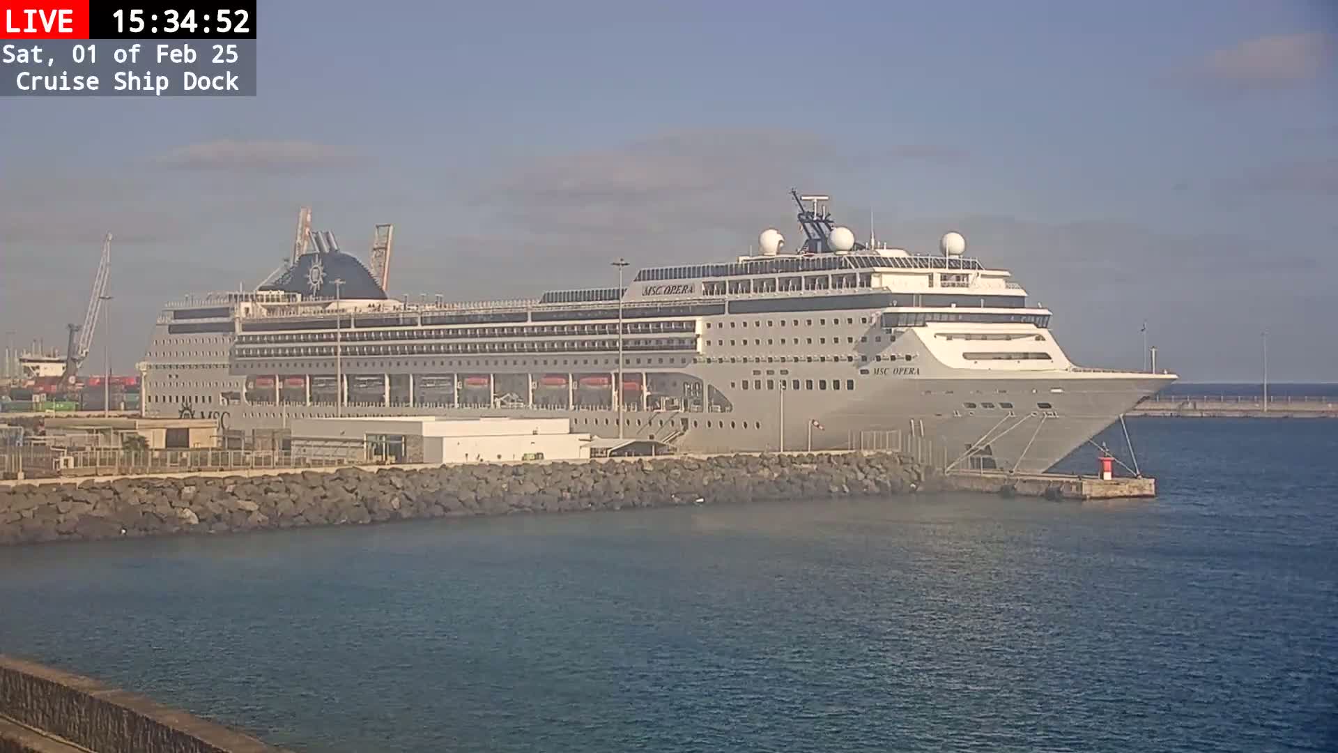 A large cruise ship is docked at a port on a calm, sunny day.