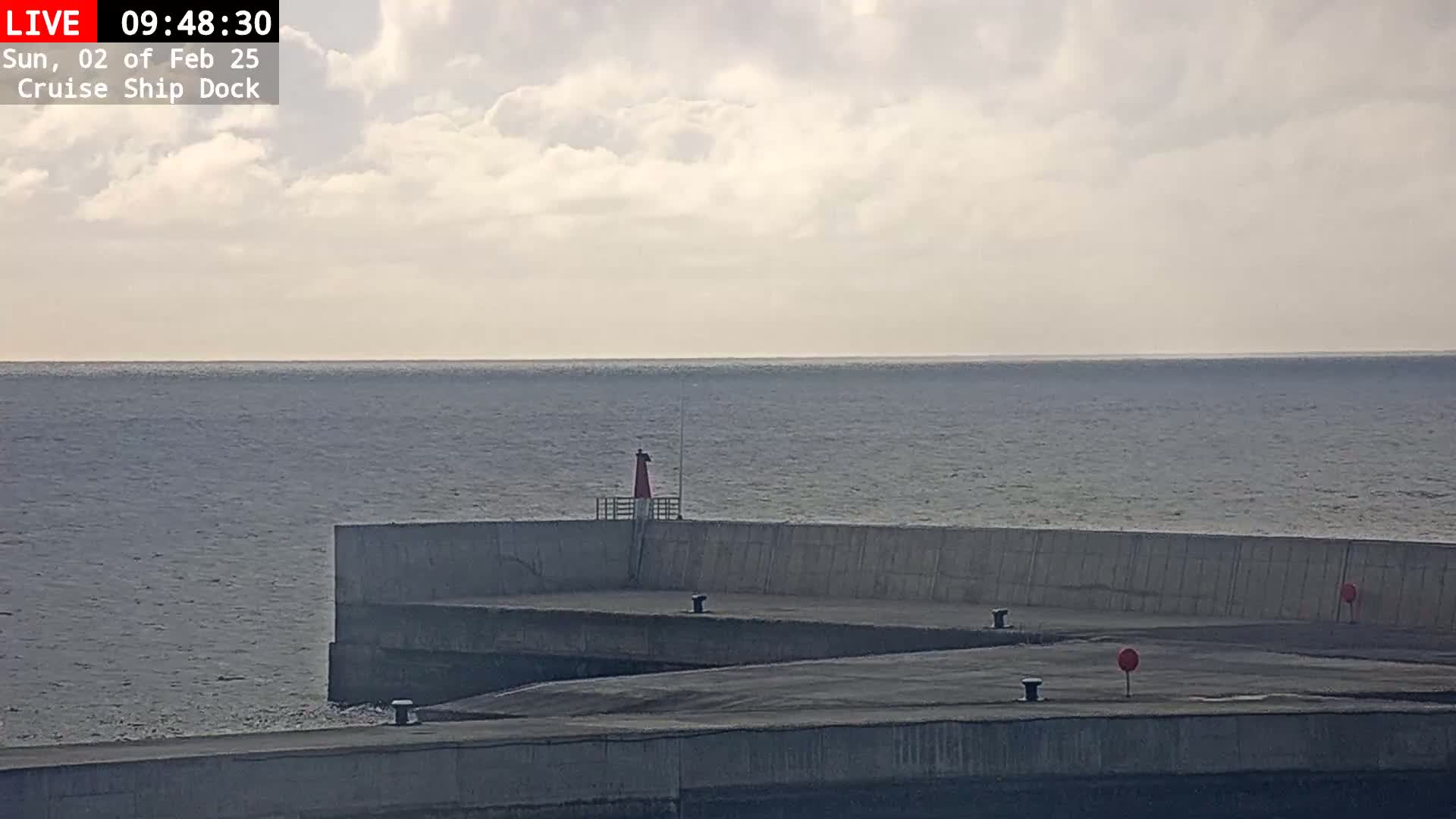 A gray concrete breakwater extends into a calm, gray ocean under a cloudy sky.