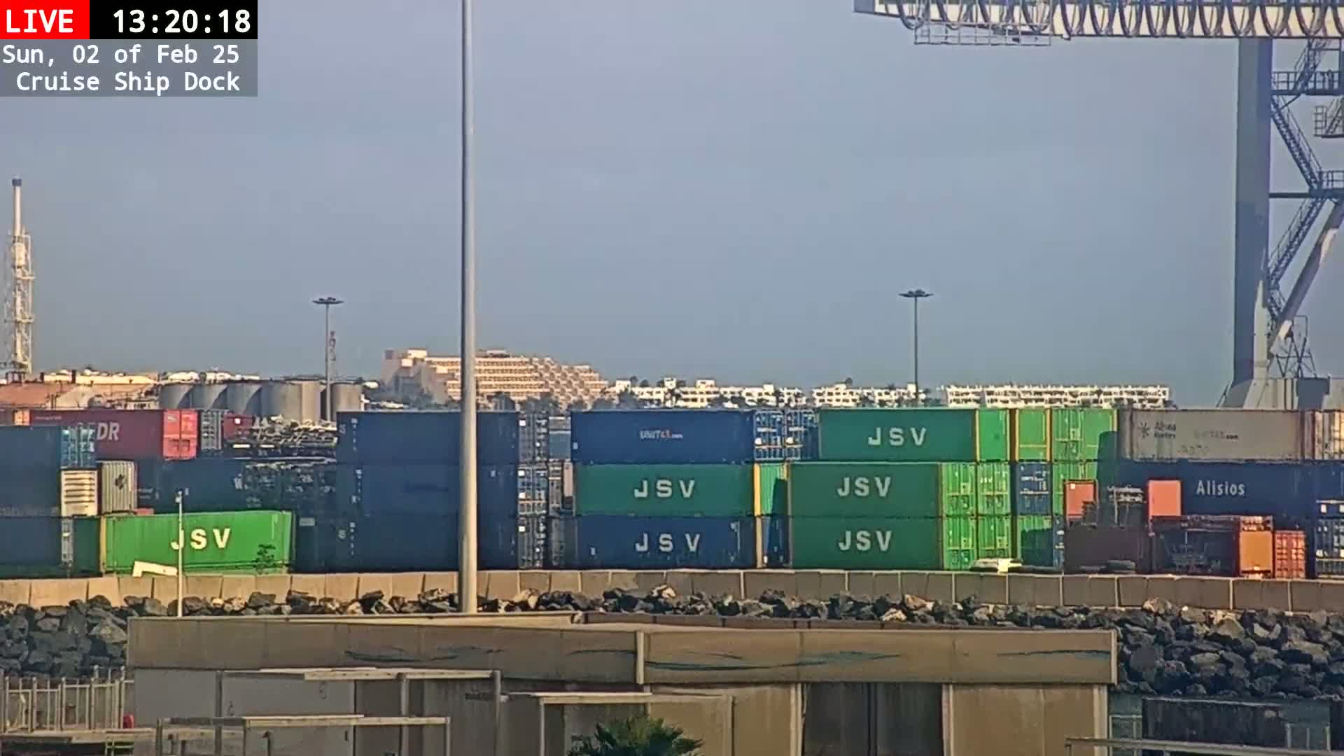 A hazy day shows a cruise ship dock with numerous stacked shipping containers, some green and others dark blue.