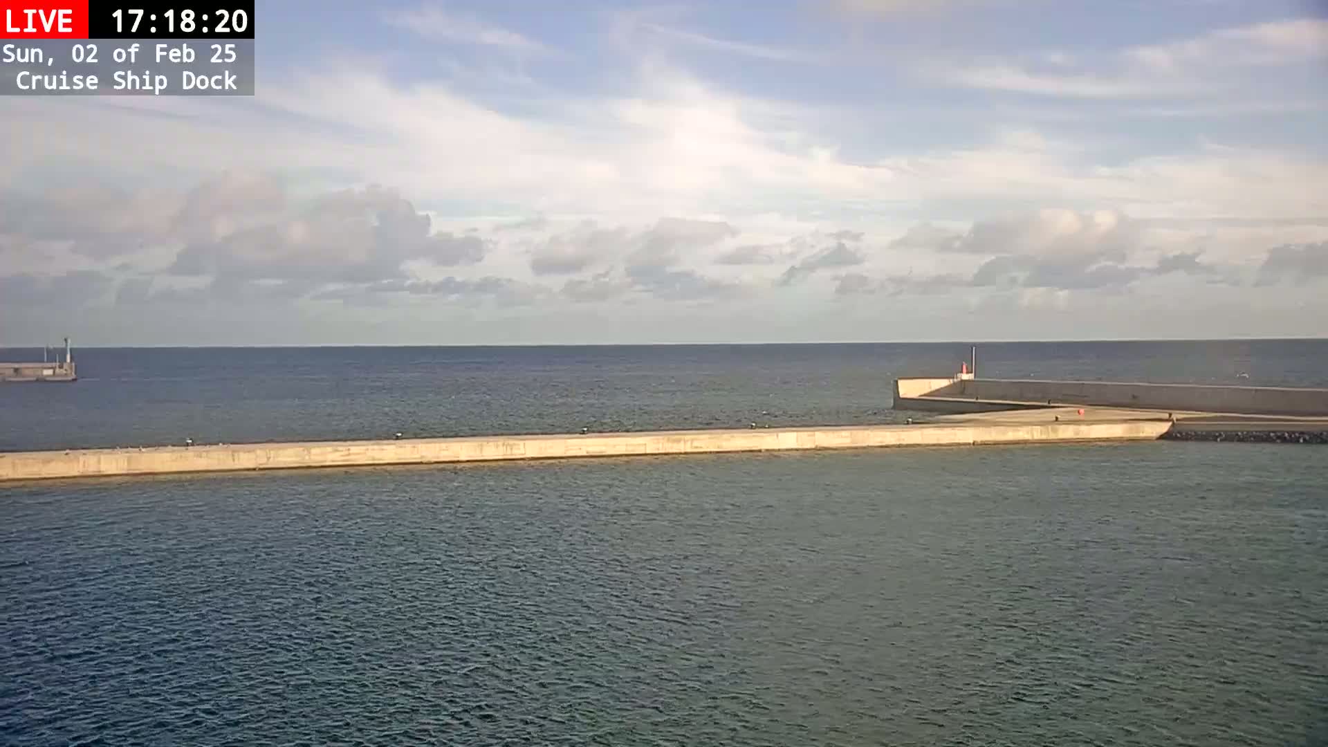 A long concrete pier extends into a calm sea under a partly cloudy sky.