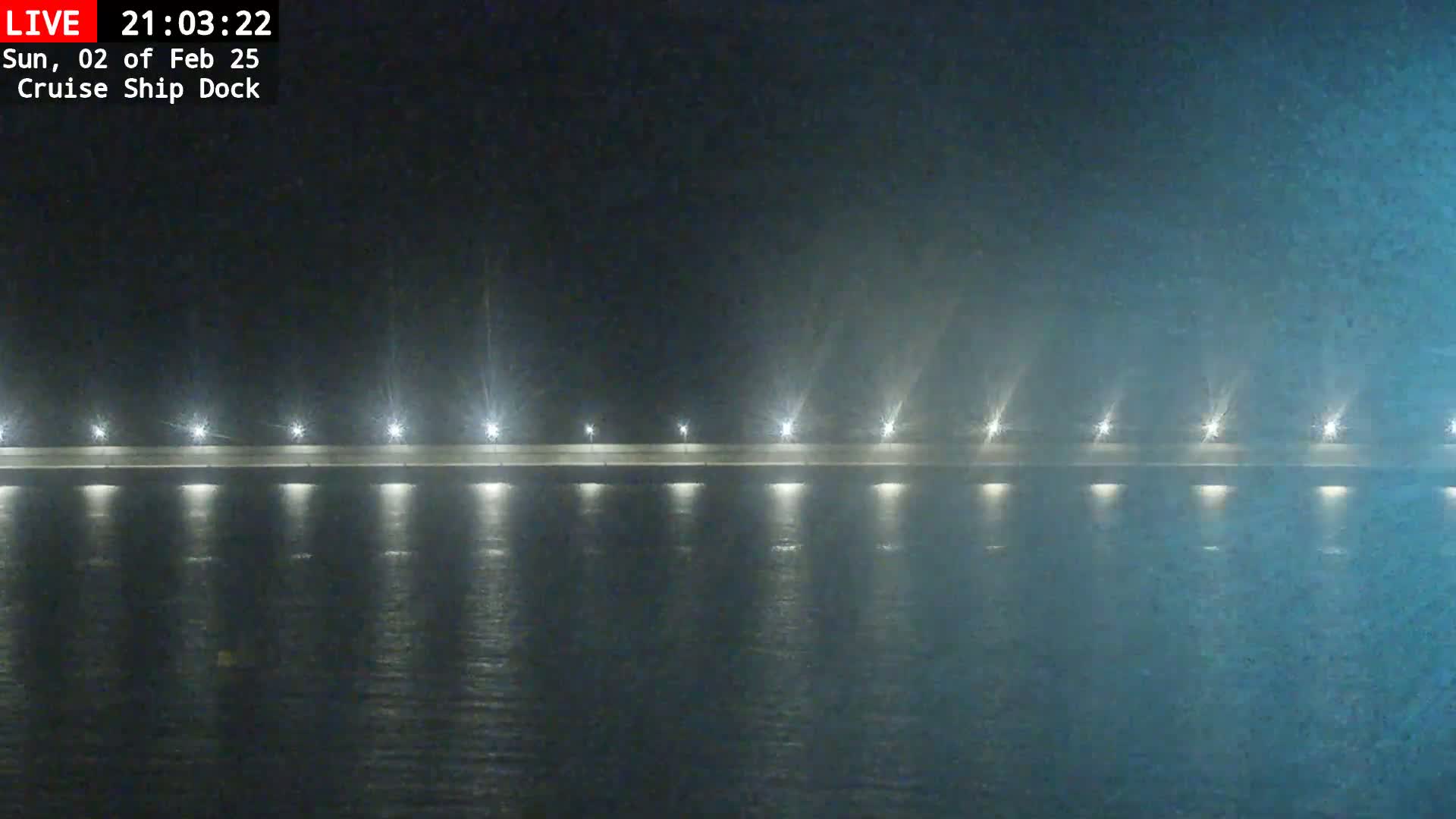 A long, low-lit dock stretches across a dark, misty body of water at night.