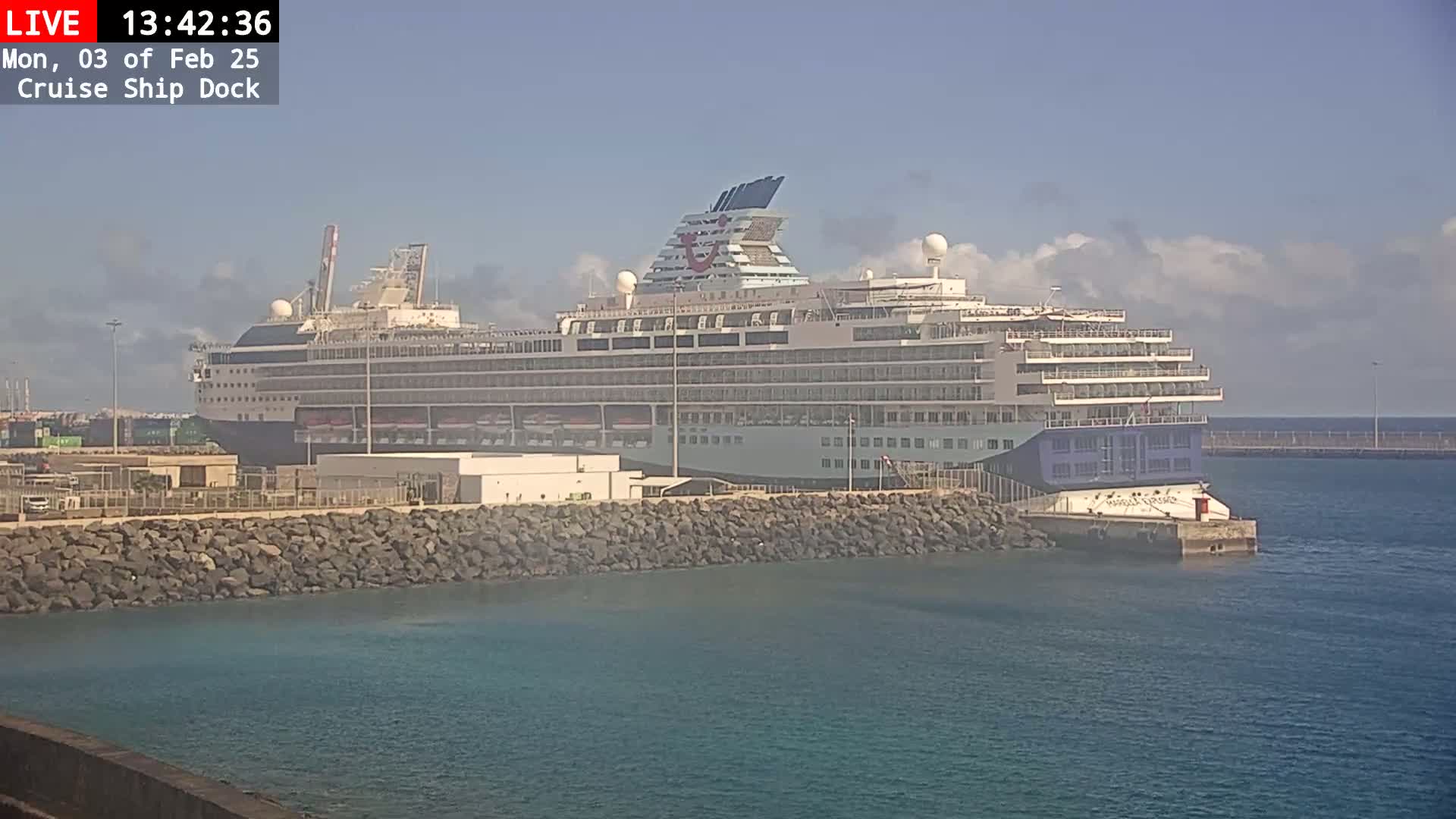 A large cruise ship is docked at a port on a partly cloudy day.