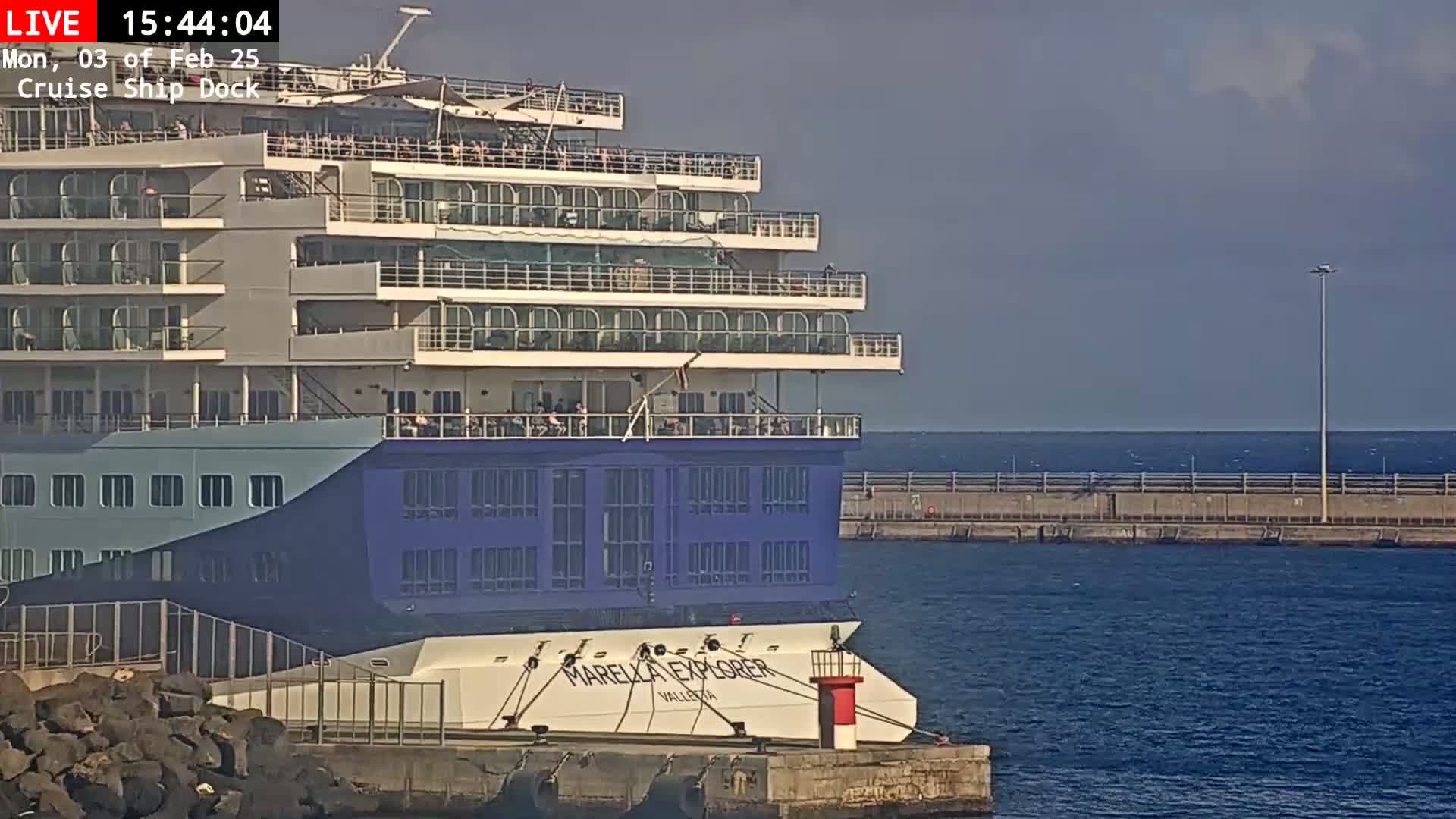 A large cruise ship is docked at a pier on a calm, sunny day.