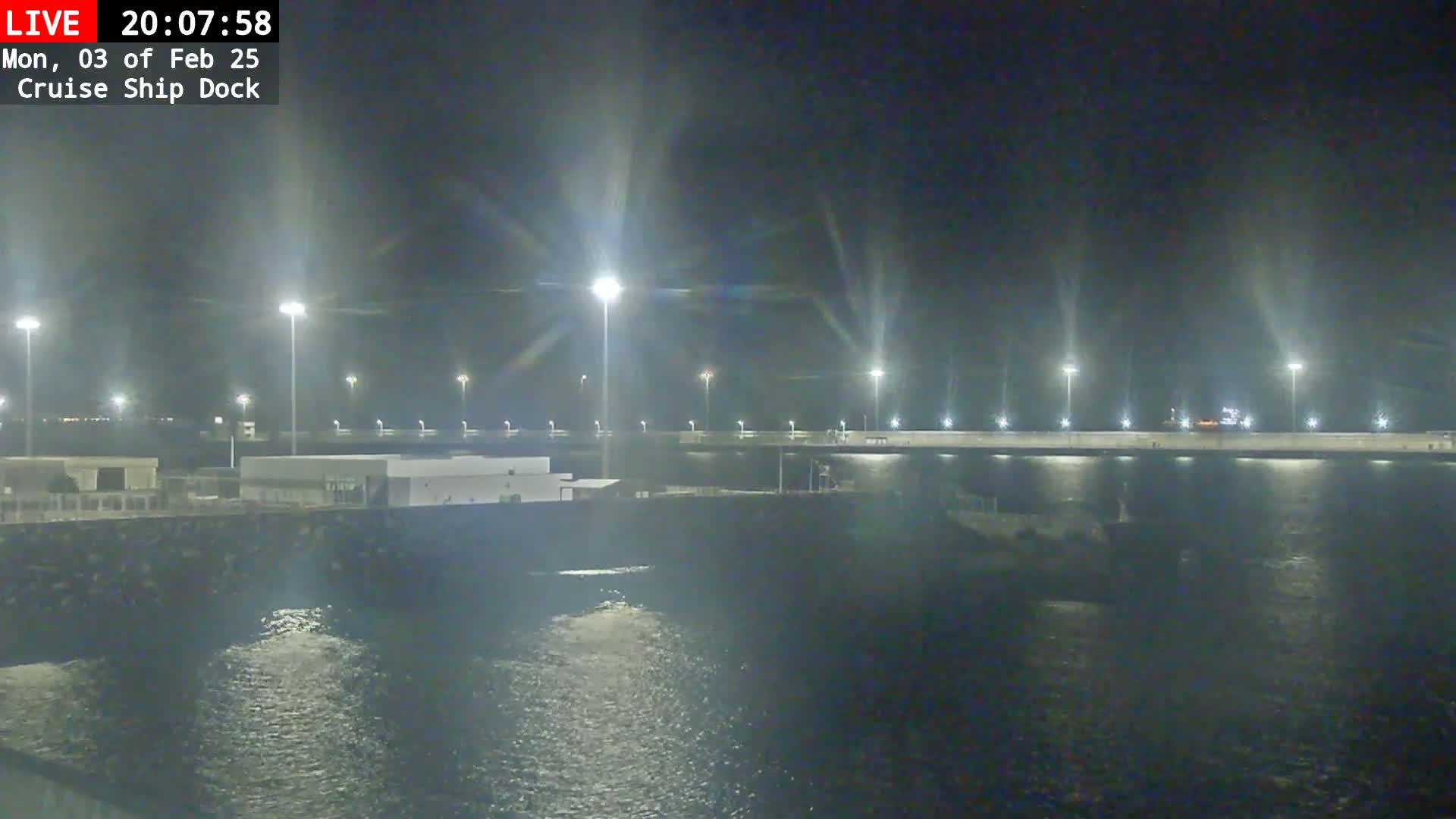 A nighttime view of a cruise ship dock with brightly lit structures and calm water.