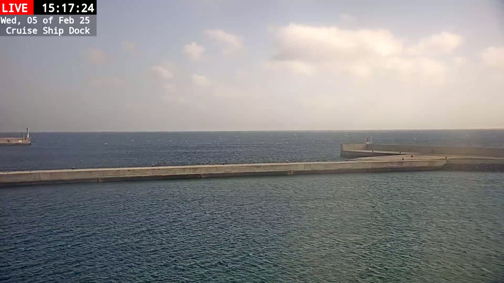 A long concrete pier extends into a calm sea under a partly cloudy sky.
