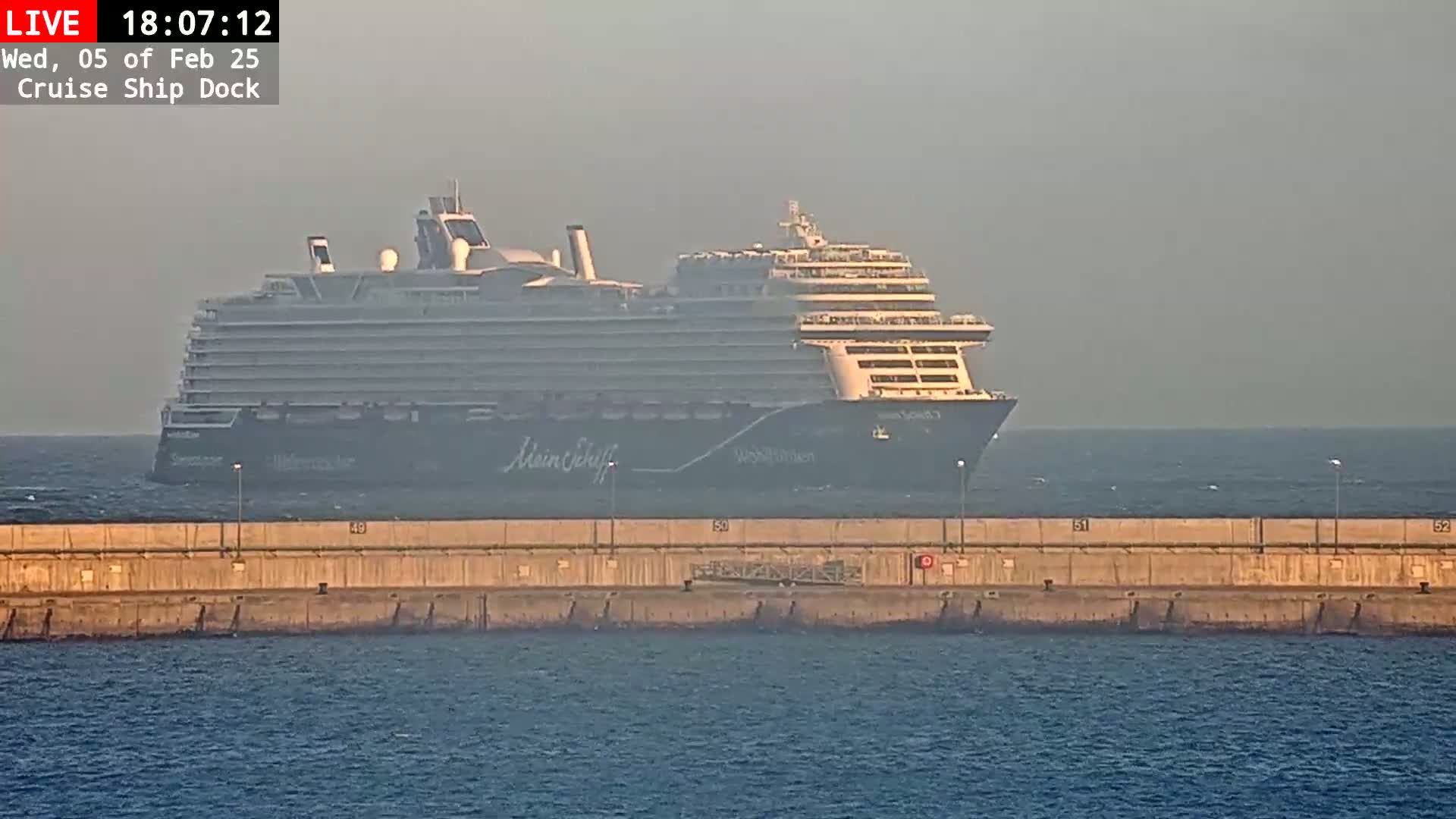 A large cruise ship is docked at a concrete pier on a hazy day.