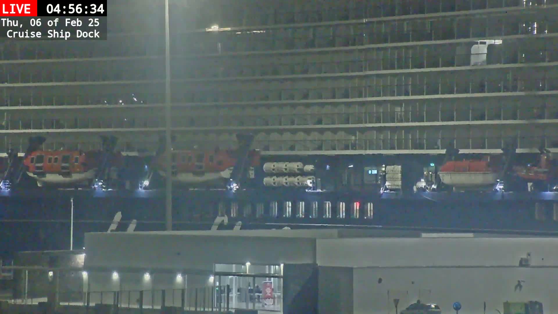 A large cruise ship is docked at night, with two lifeboats visible at the waterline.