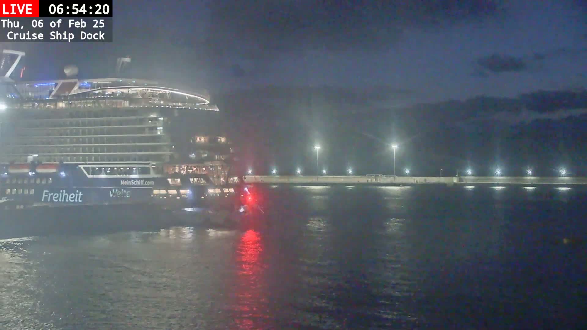 A large cruise ship is docked at night next to a lit pier in calm water.