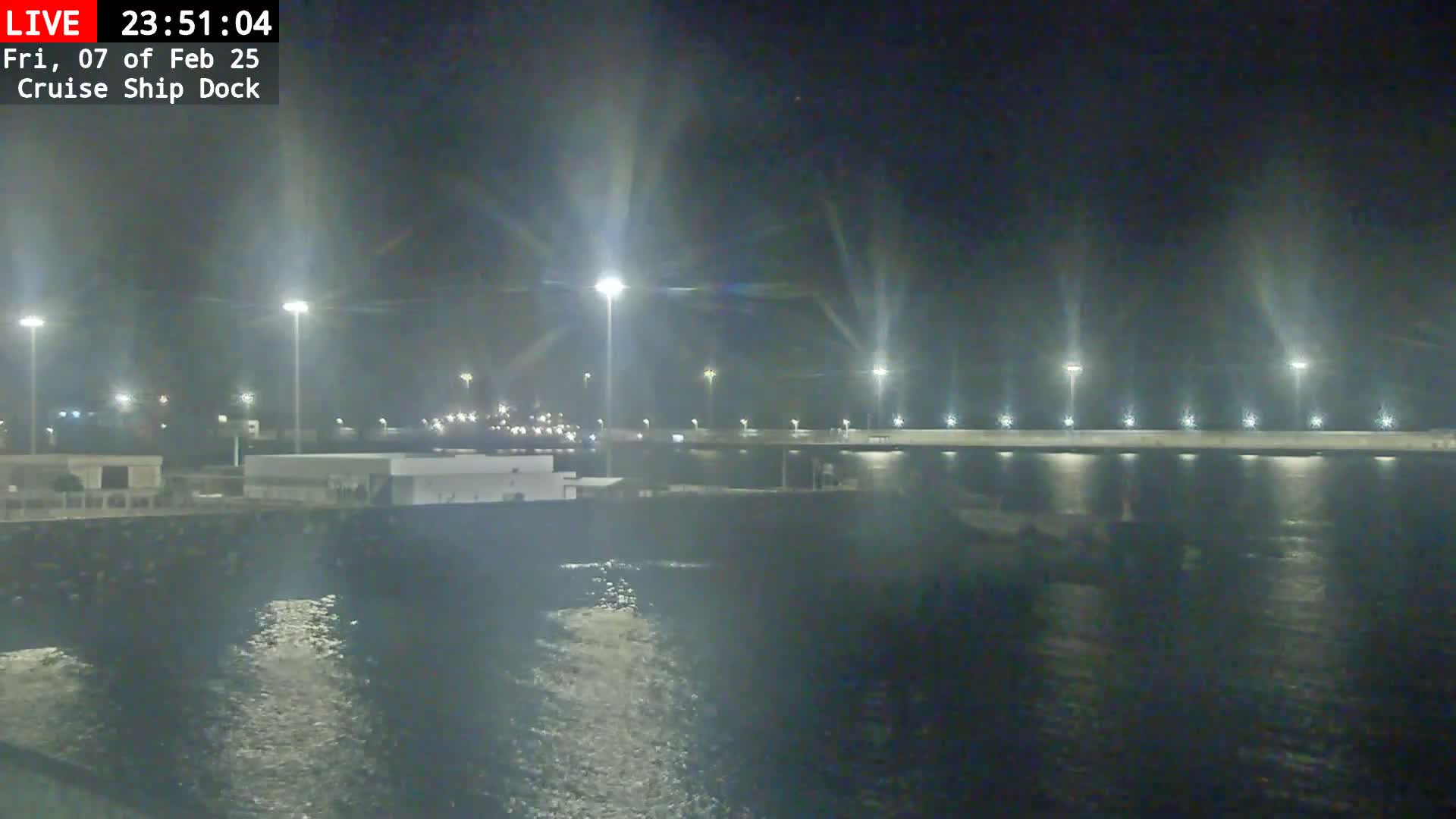A nighttime view of a cruise ship dock with calm water and bright lights illuminating the area.