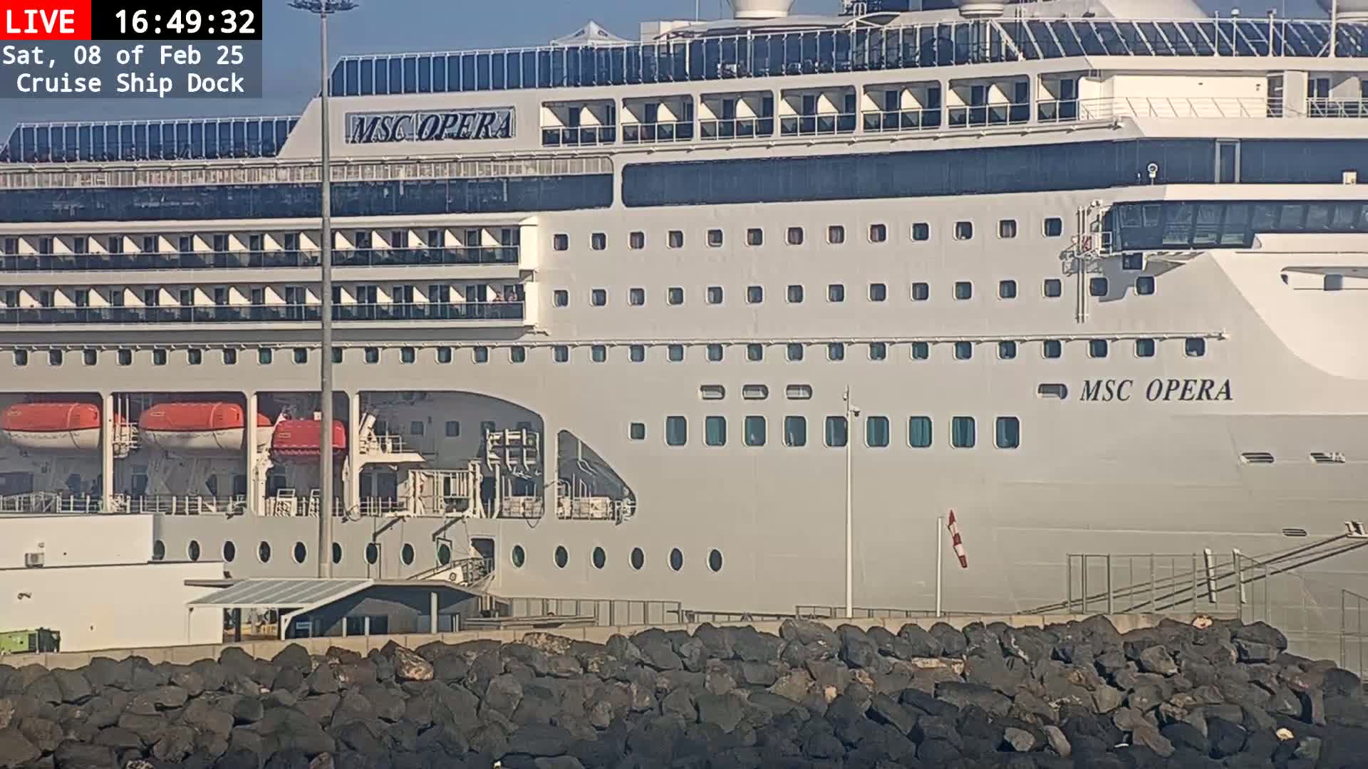 A large cruise ship, the MSC Opera, is docked at a port on a sunny day.