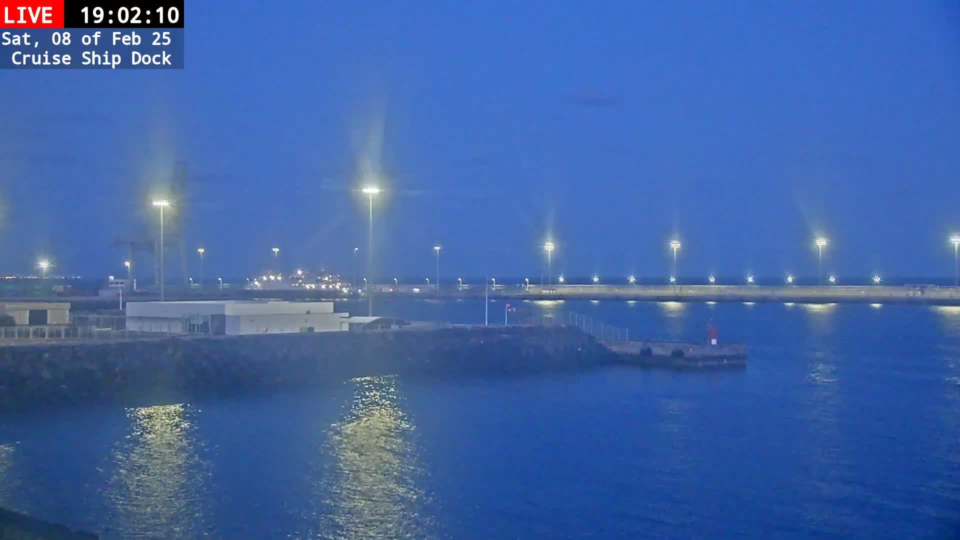 A nighttime view of a cruise ship dock, illuminated by numerous lights, with calm, dark blue water reflecting the lights.
