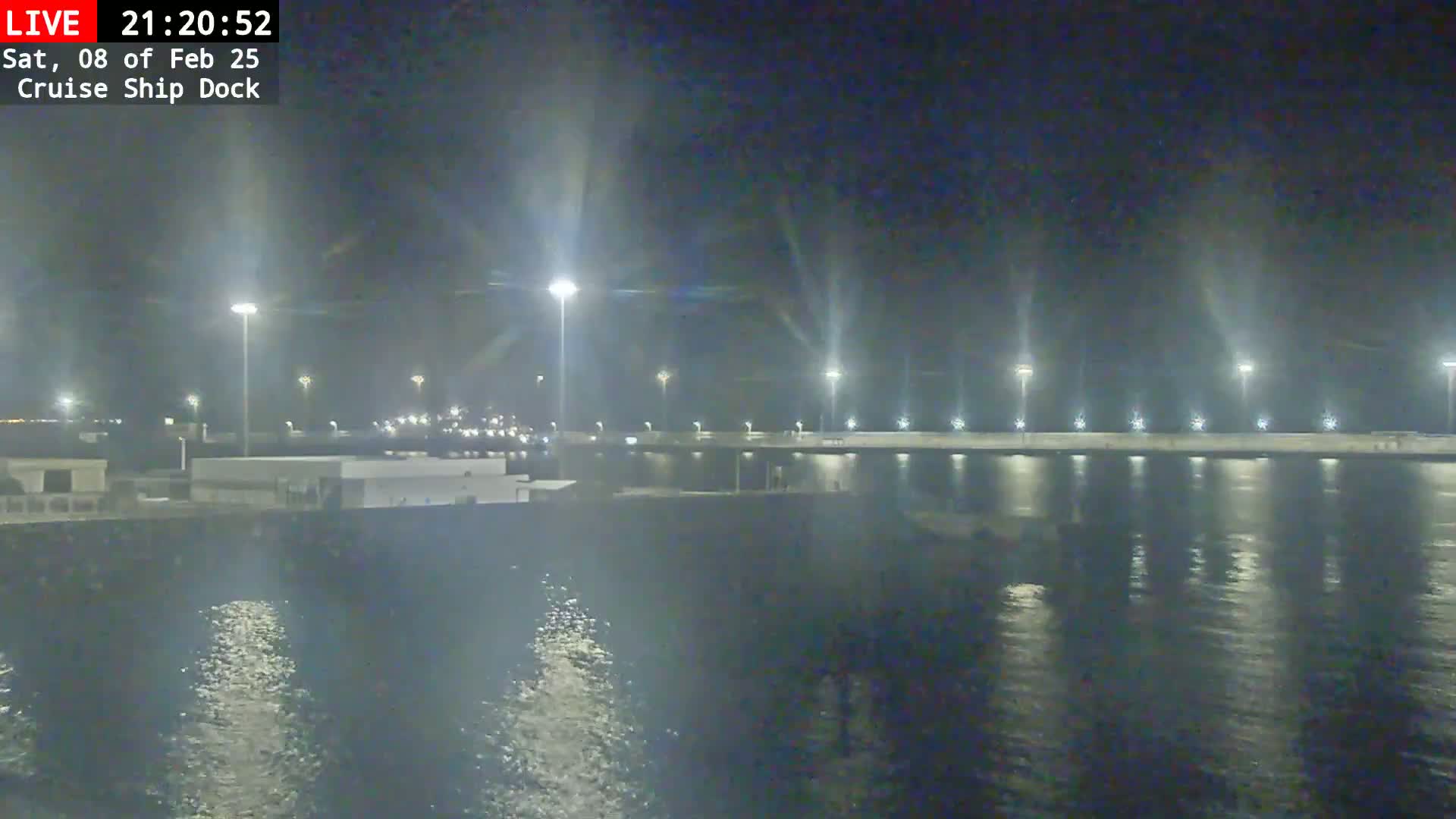 A nighttime view of a cruise ship dock illuminated by bright lights, reflecting on calm water.