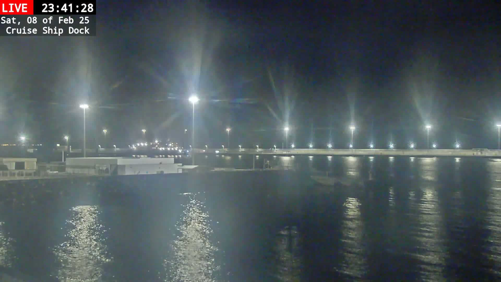 A nighttime view of a brightly lit cruise ship dock and calm water reflecting the lights.