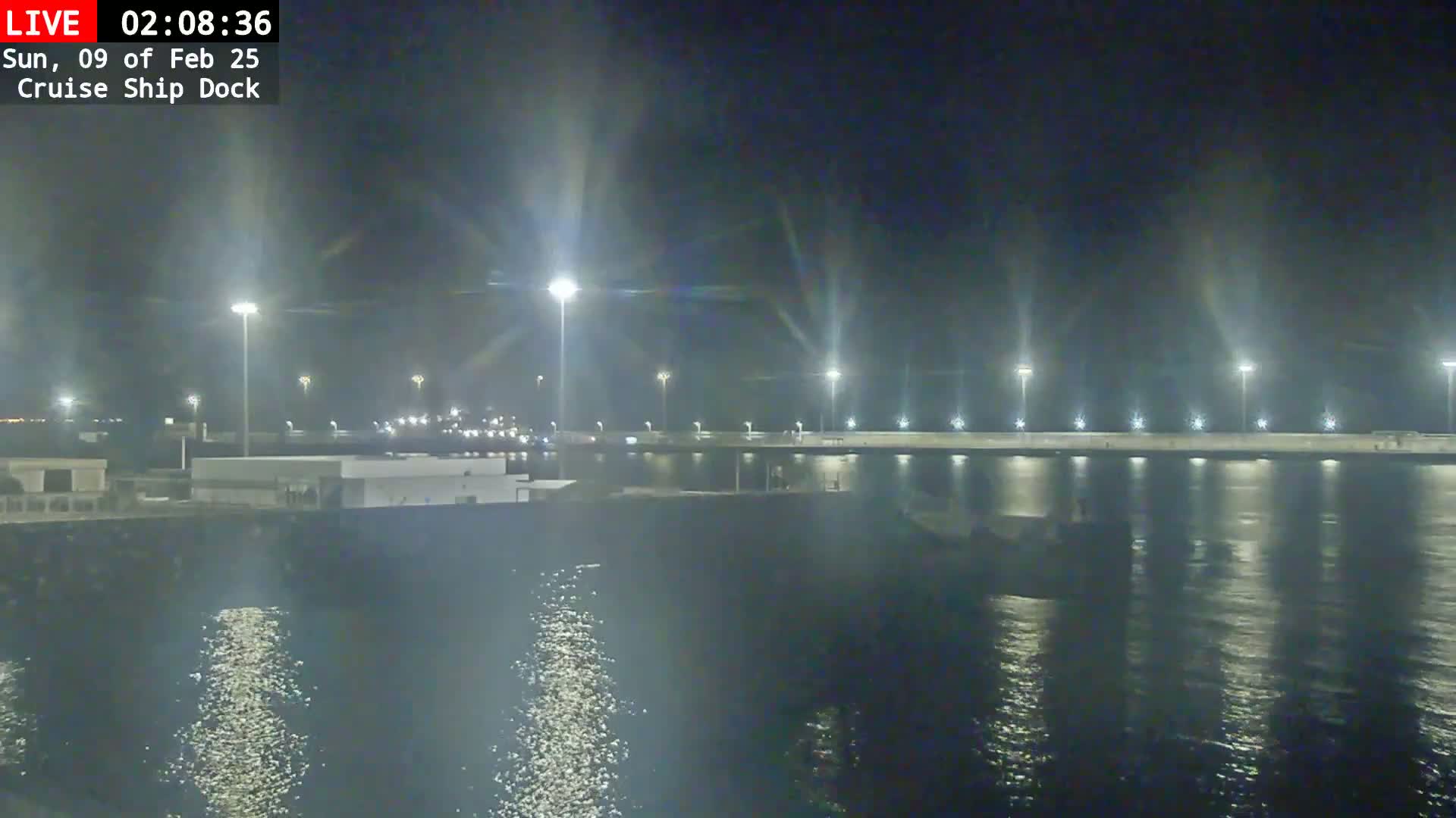 A nighttime view of a calm body of water reflecting the lights of a cruise ship dock.