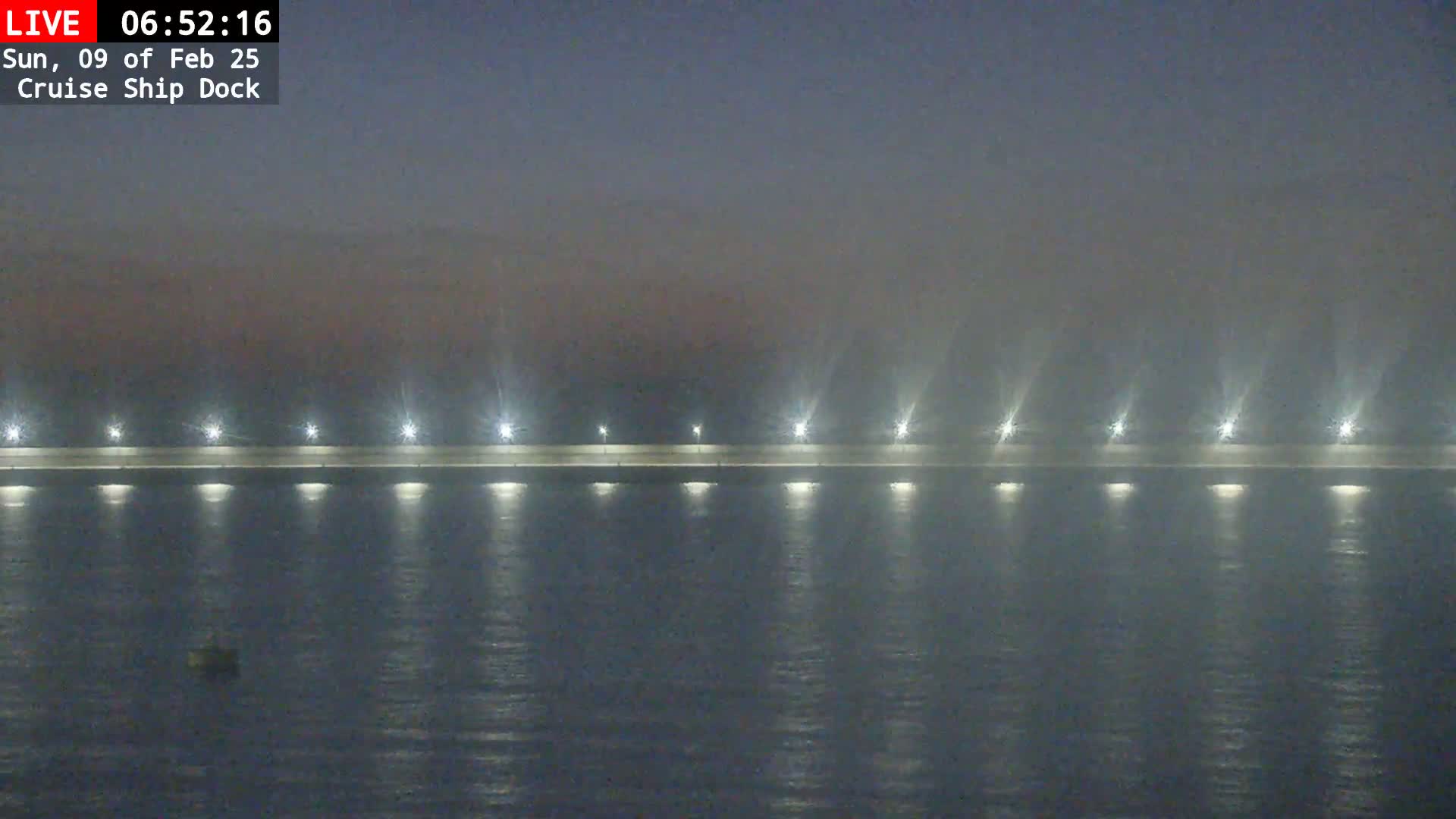 A long, illuminated dock stretches across a foggy body of water at night.