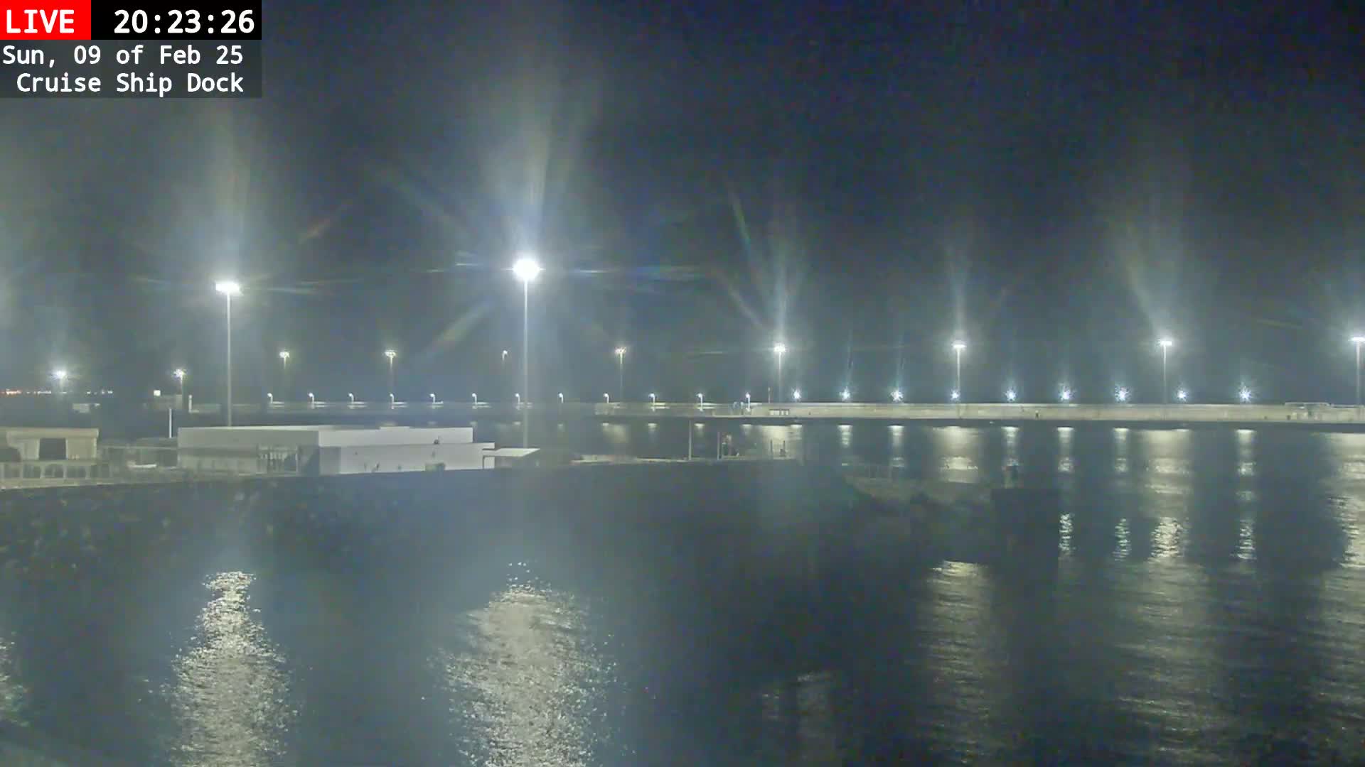 A nighttime view of a cruise ship dock illuminated by bright lights, reflecting on calm water.