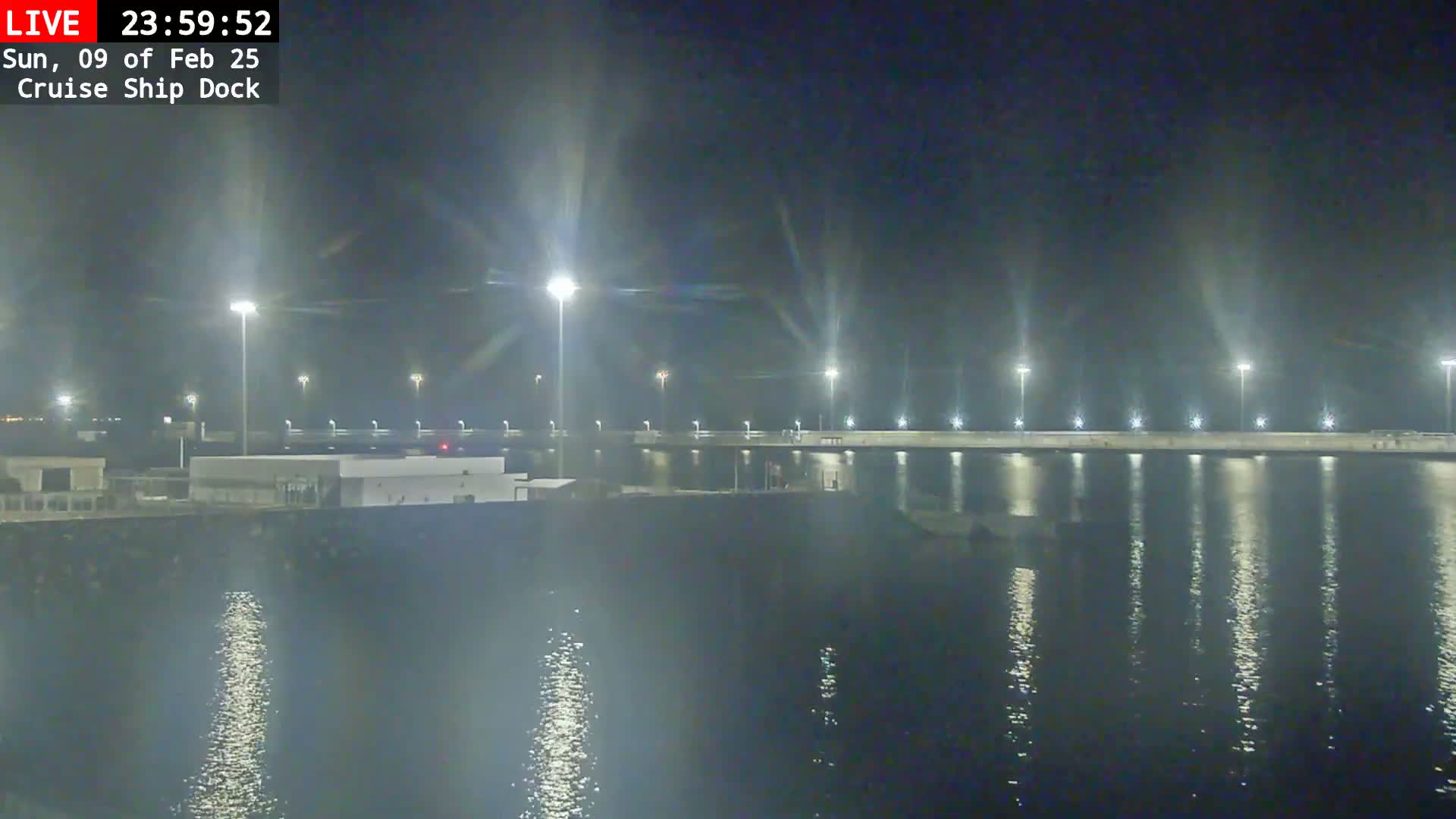 A nighttime view of a cruise ship dock illuminated by numerous lights, reflecting on the calm water.