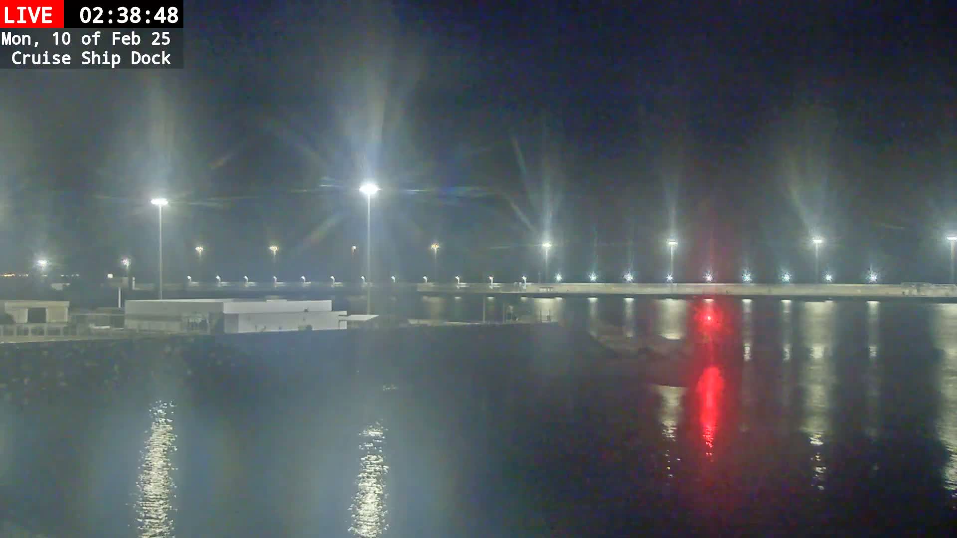 A nighttime view of a calm body of water reflecting the lights of a dock and buildings.