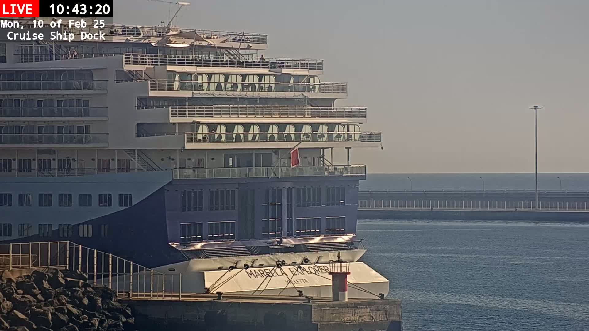 A large cruise ship is docked at a pier on a sunny day with calm water.